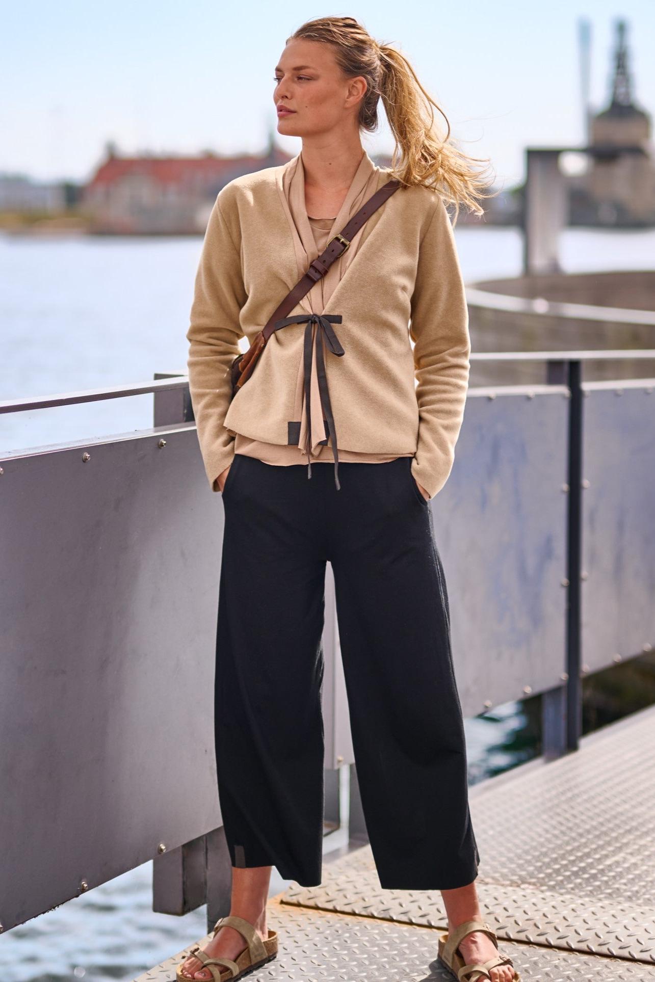 Woman wearing a beige Henriette Steffensen cardigan and black pants standing on a harbor walkway