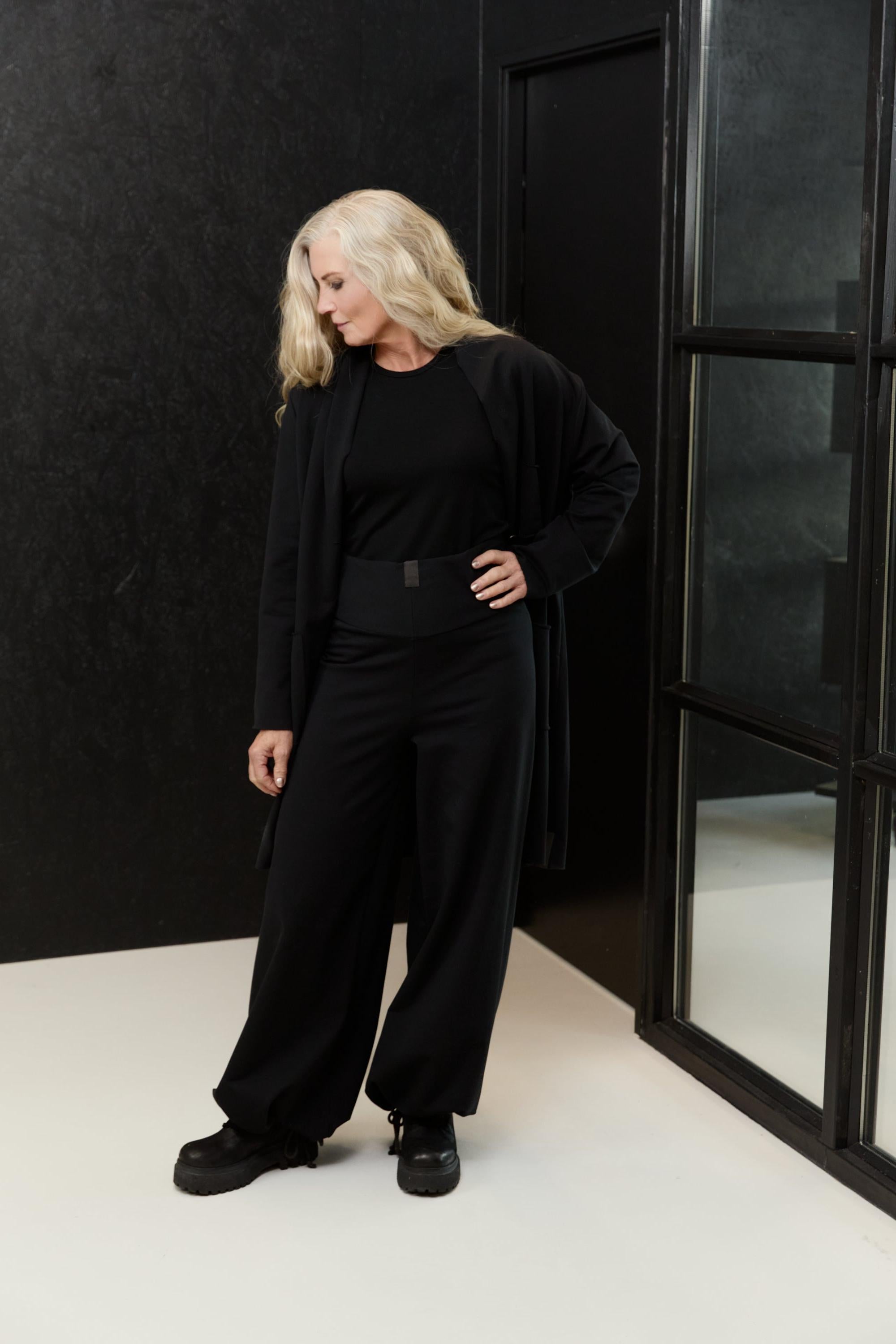 A woman wearing a Henriette Steffensen black blazer and matching trousers in a studio setting.