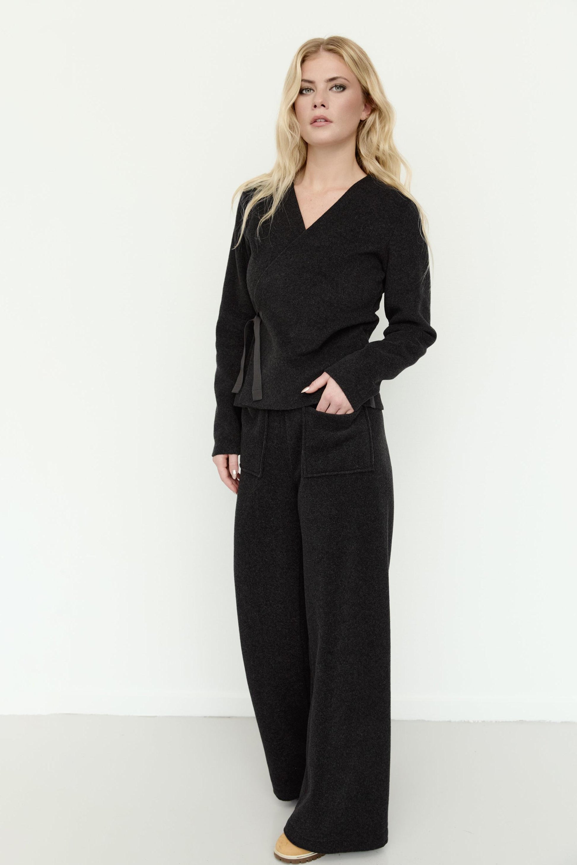 A blonde woman wearing a Henriette Steffensen black fleece wrap top and matching wide-leg trousers.