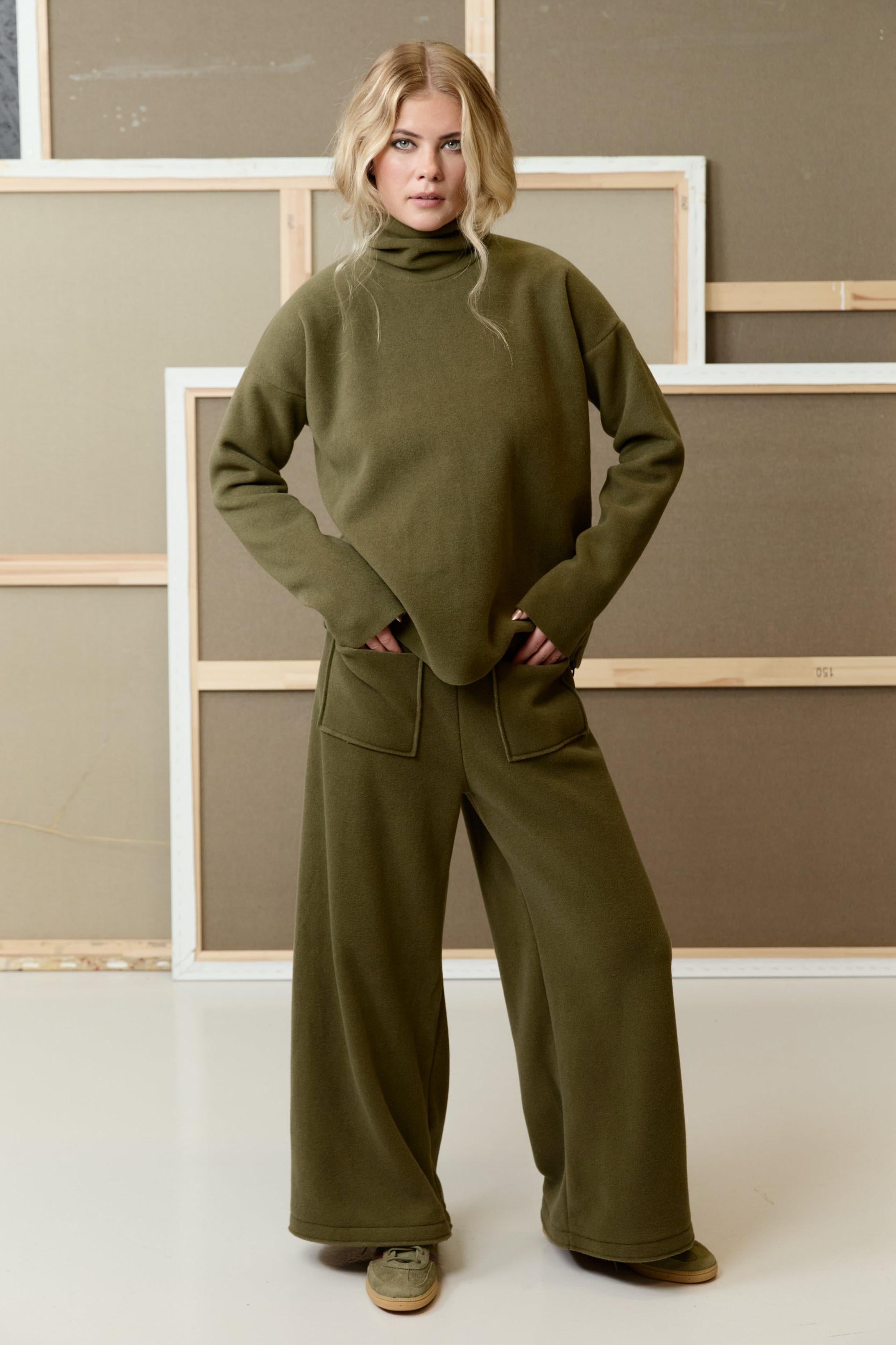 A woman wearing a stylish olive green fleece top and wide-leg trousers by Henriette Steffensen.