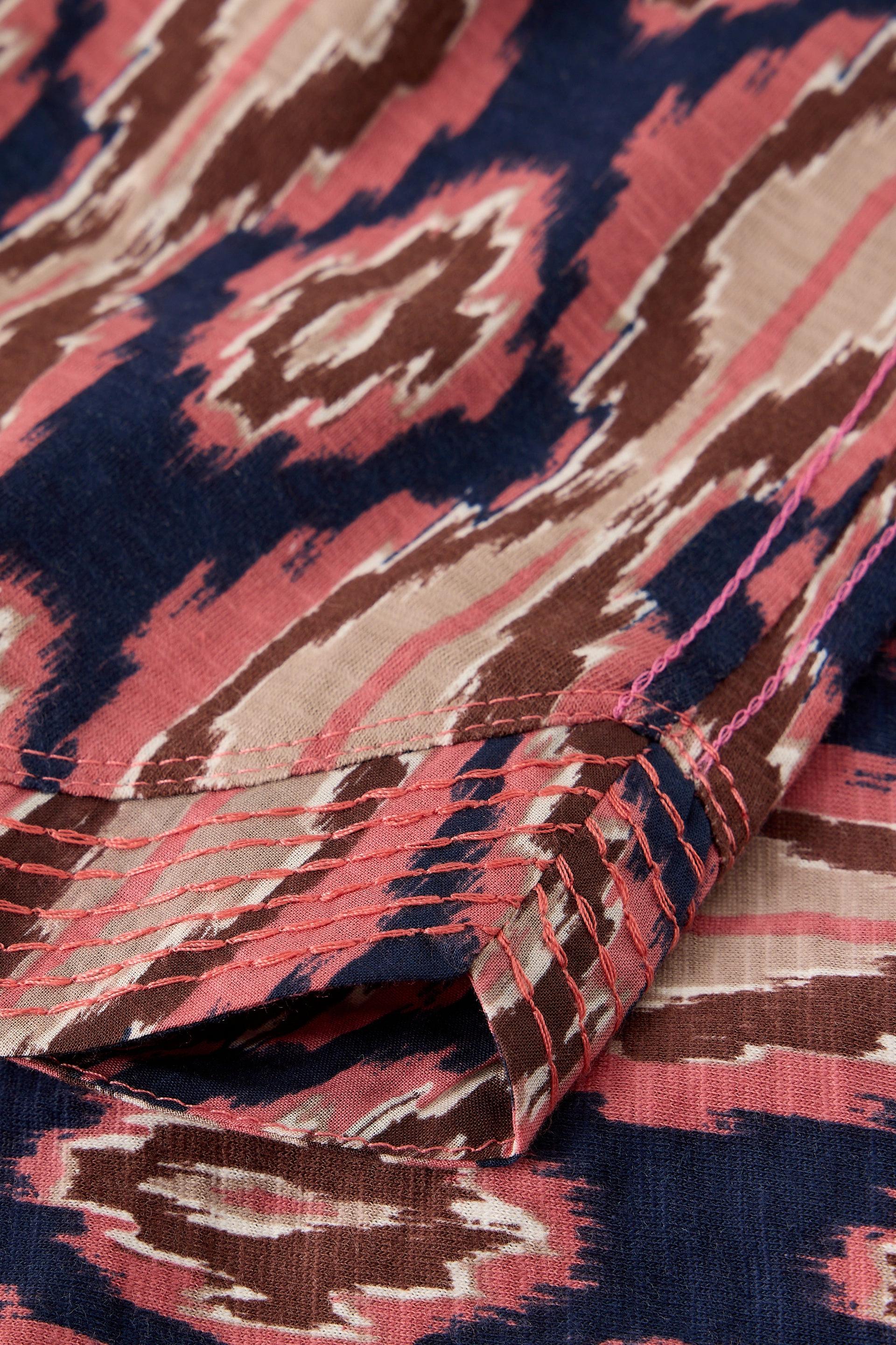 A close-up of patterned fabric with an ikat-style design in navy blue, dusty pink, and beige, showing a folded corner that reveals the texture and stitching.