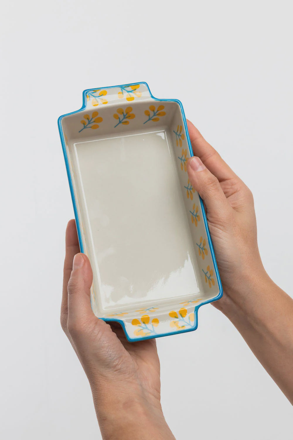 Rectangular ceramic baking dish with floral patterns held by a person on a white background