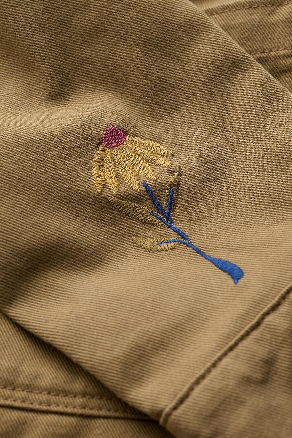 Close-up of a floral embroidery detail on a khaki Seasalt organic cotton jacket.
