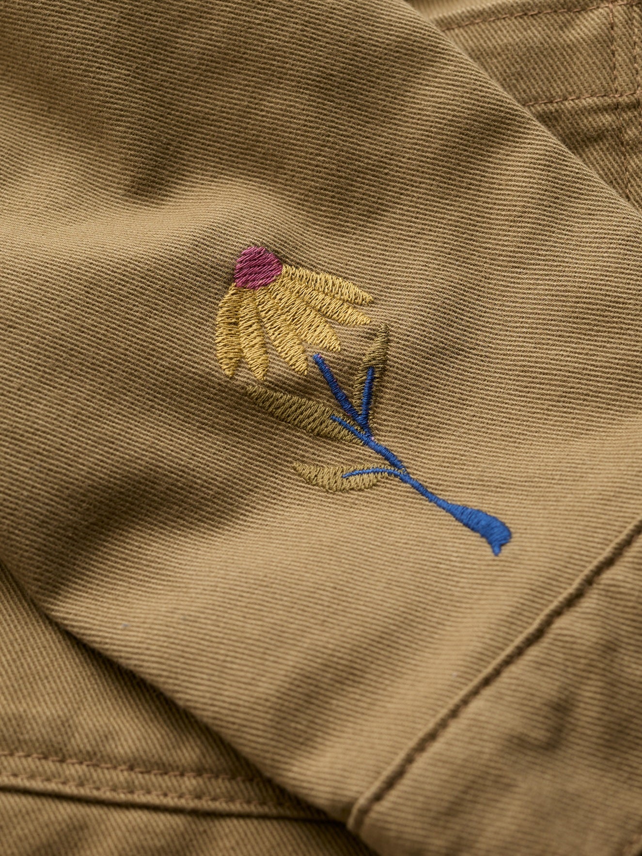 Close-up of a floral embroidery detail on a khaki Seasalt organic cotton jacket.