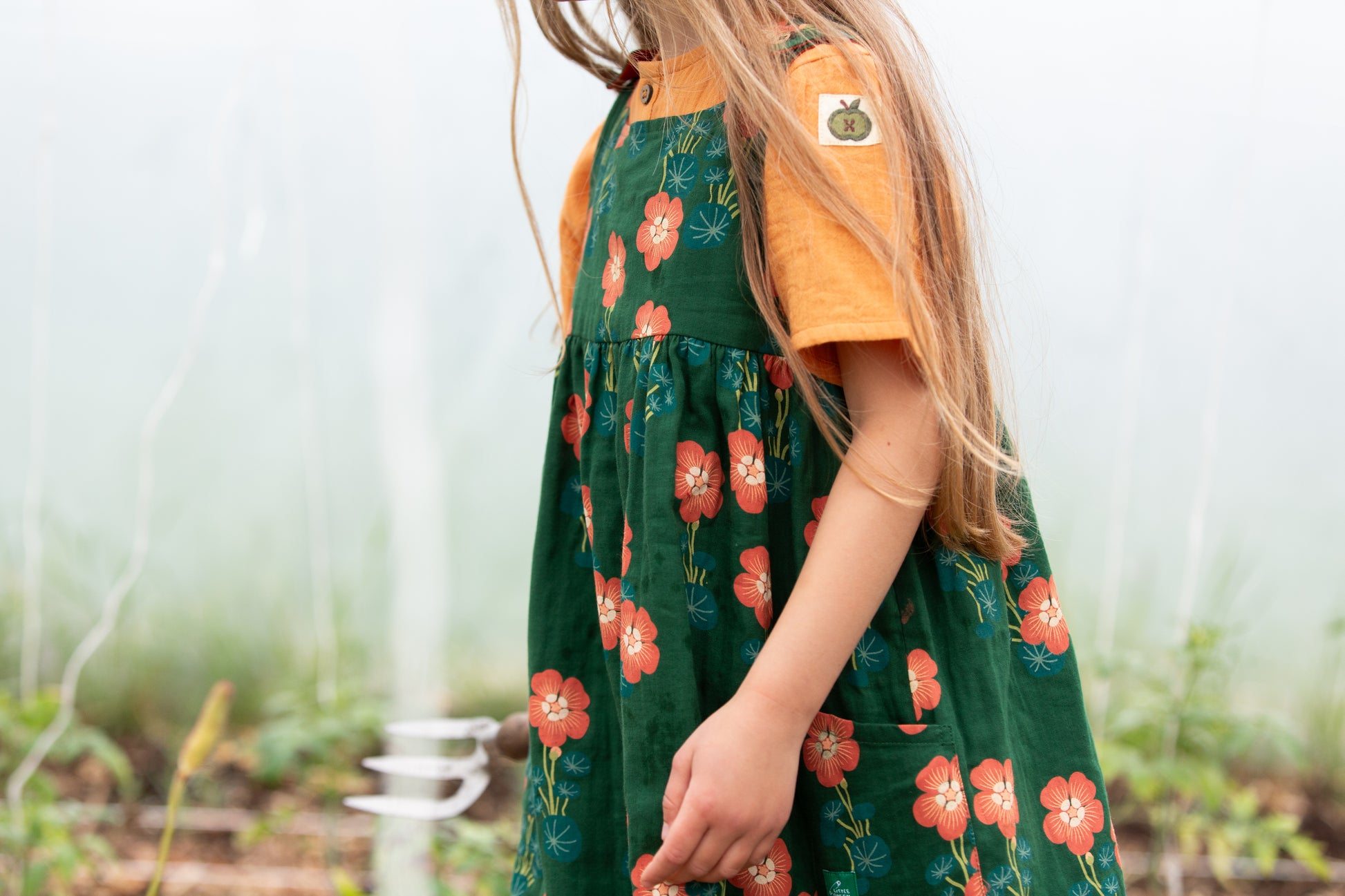 Child wearing a green floral dress with an orange shirt in a garden setting