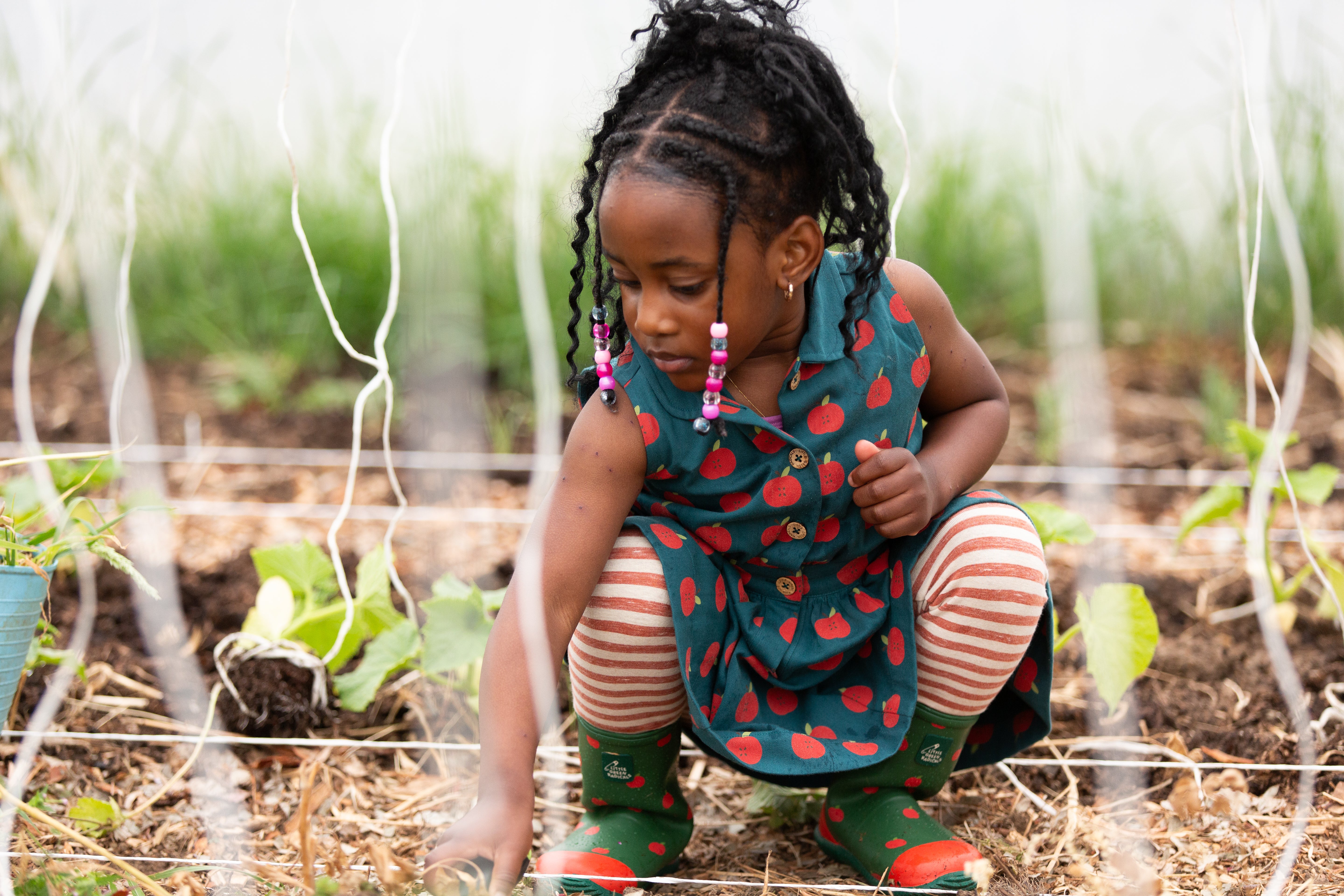 Child in a garden wearing a colourful dress, organic cotton striped leggings and rain boots.
