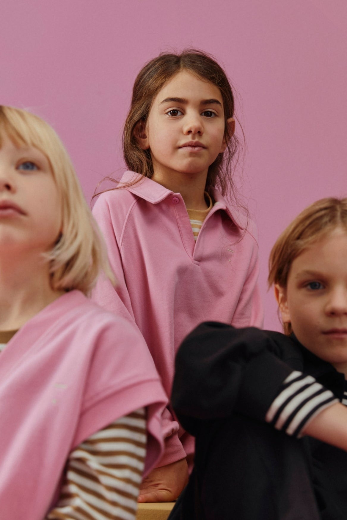 Three children wearing pink and striped clothing posed against a solid pink background.