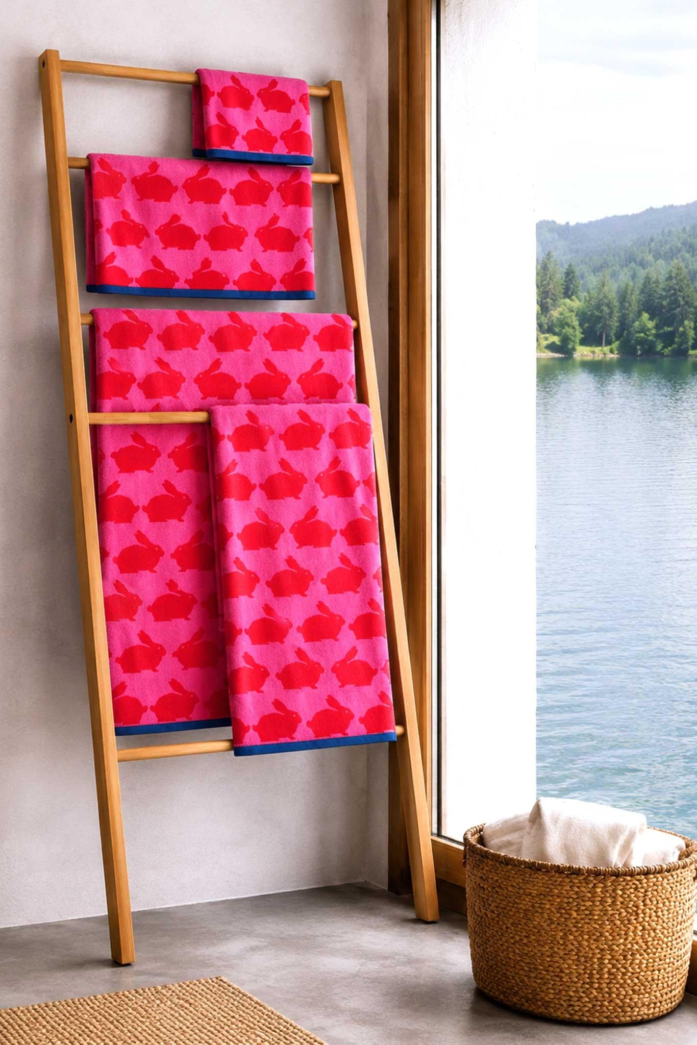 Pink patterned towels on a wooden ladder by a window with a view of water and trees.