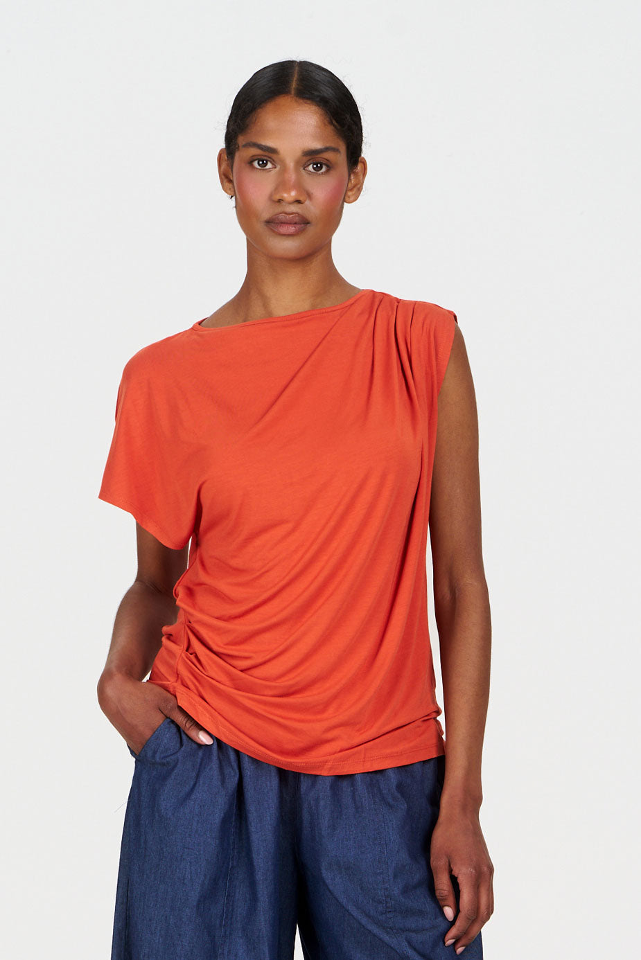 Woman wearing a Komodo orange top and blue pants on a white background