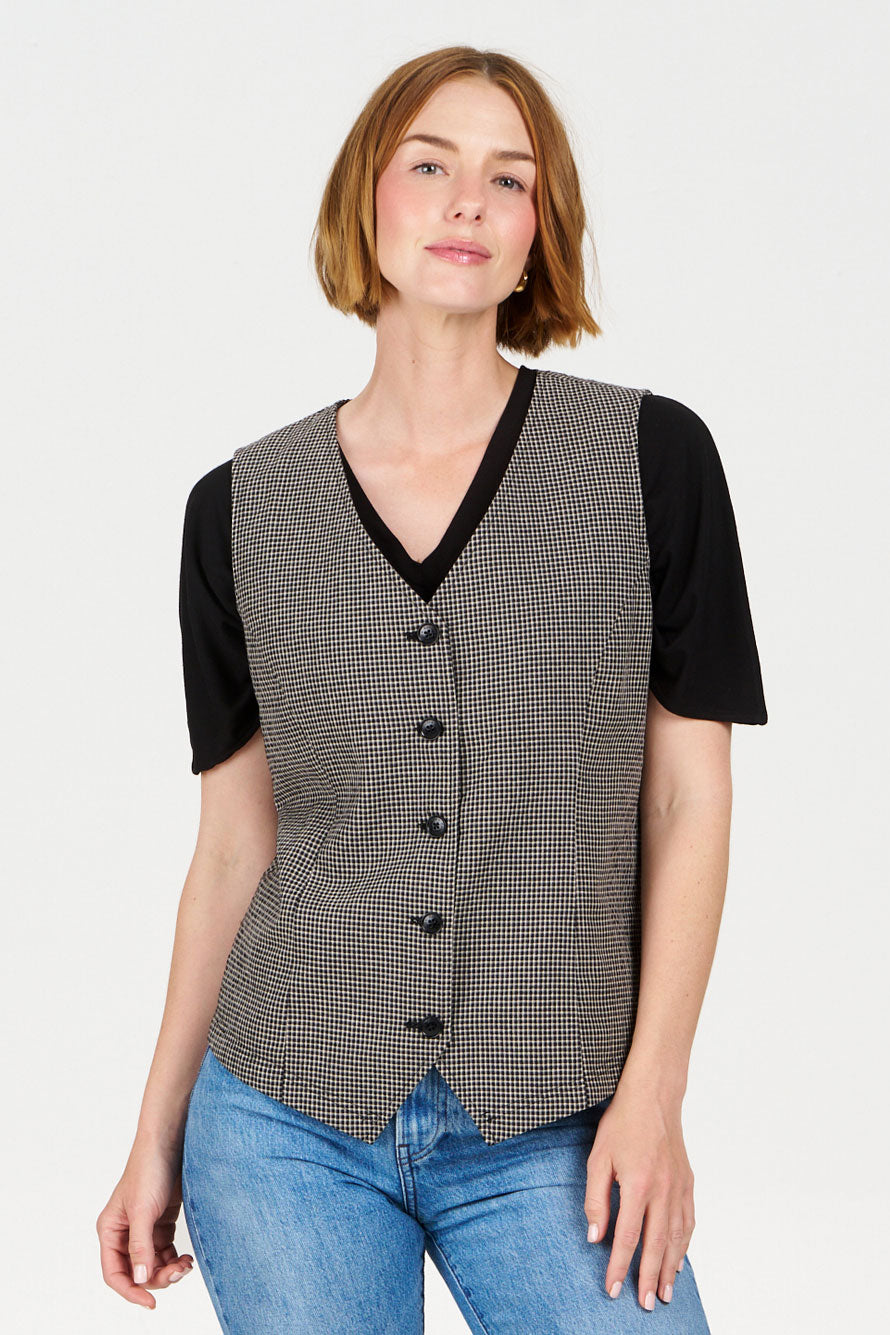 Woman wearing a patterned Komodo vest over a black shirt with blue jeans on a white background