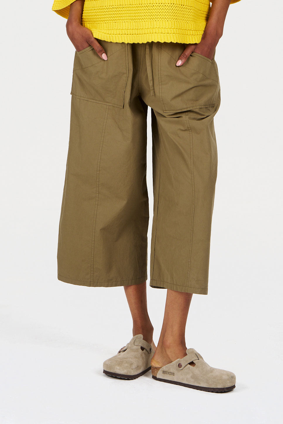 Person wearing green wide-leg pants and beige shoes on a white background