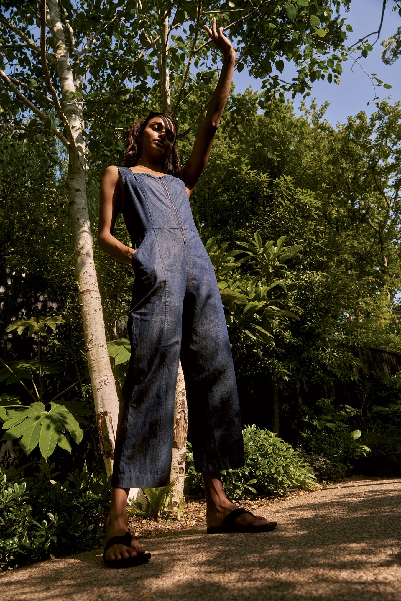Woman in a denim jumpsuit standing in a forested area