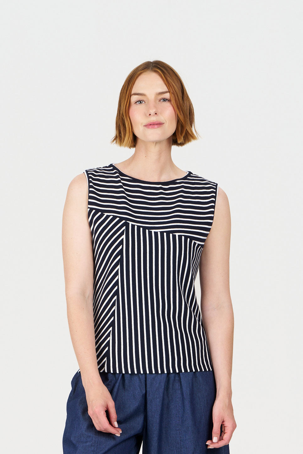 Woman wearing a navy and white striped sleeveless top with blue pants on a light gray background