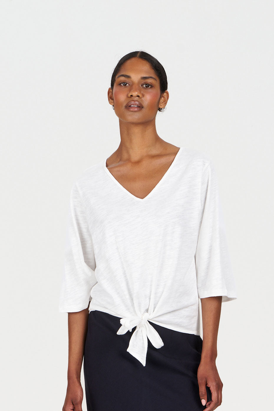 Woman wearing a white organic cotton top with a knot detail and black pants on a white background