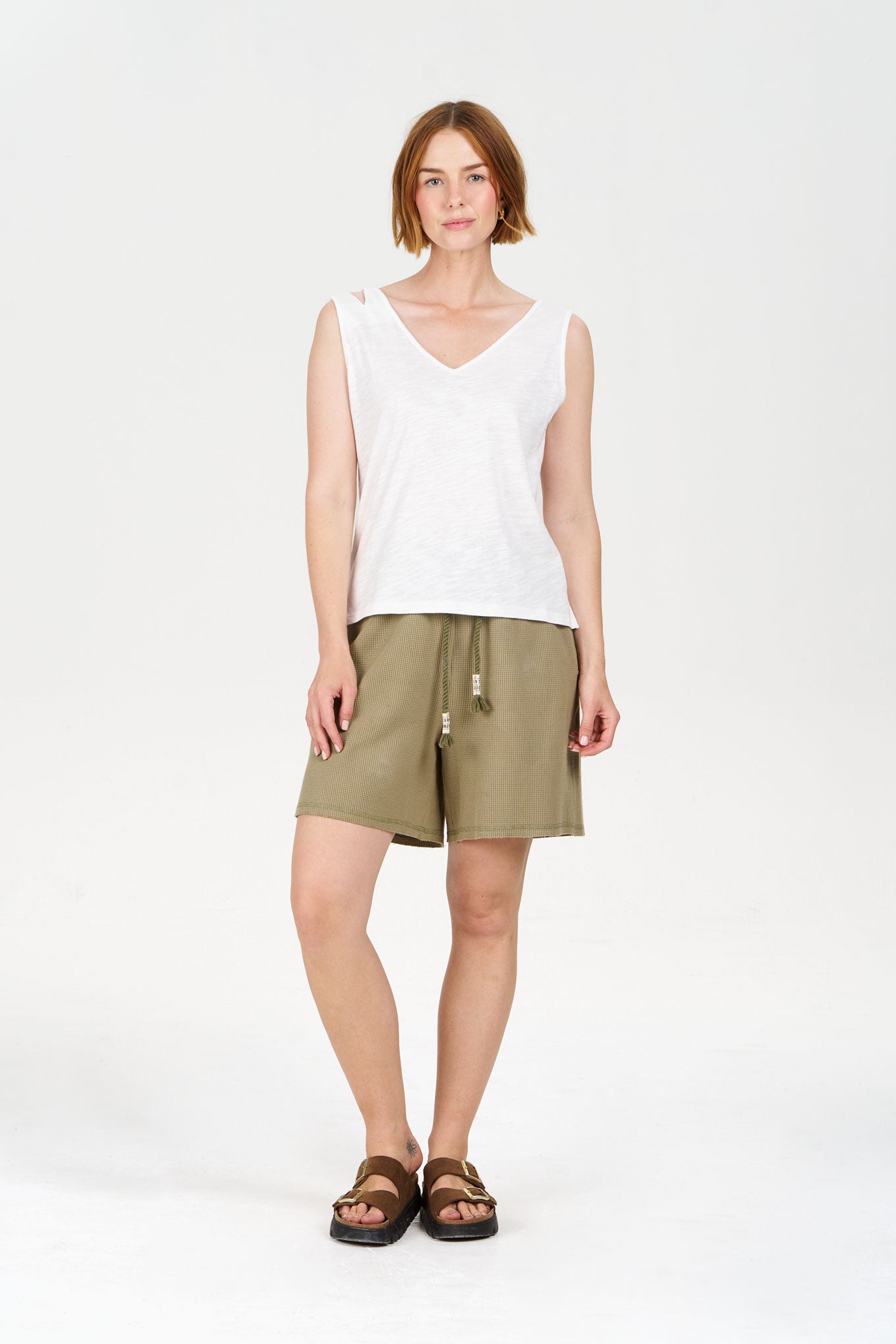Woman wearing a white sleeveless top and olive green shorts on a white background