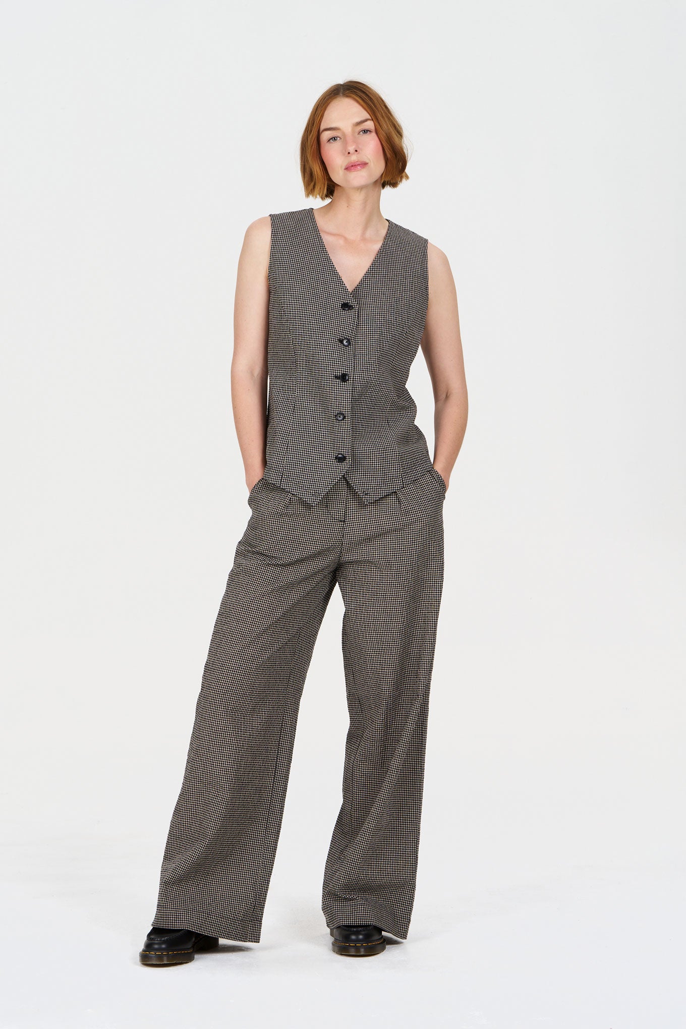 Woman wearing a checkered suit vest and pants on a white background