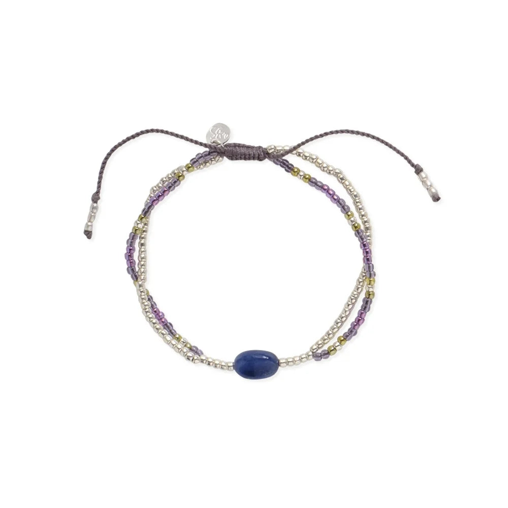 A delicate layered bracelet featuring a deep blue lapis lazuli gemstone and small metallic and purple beads.