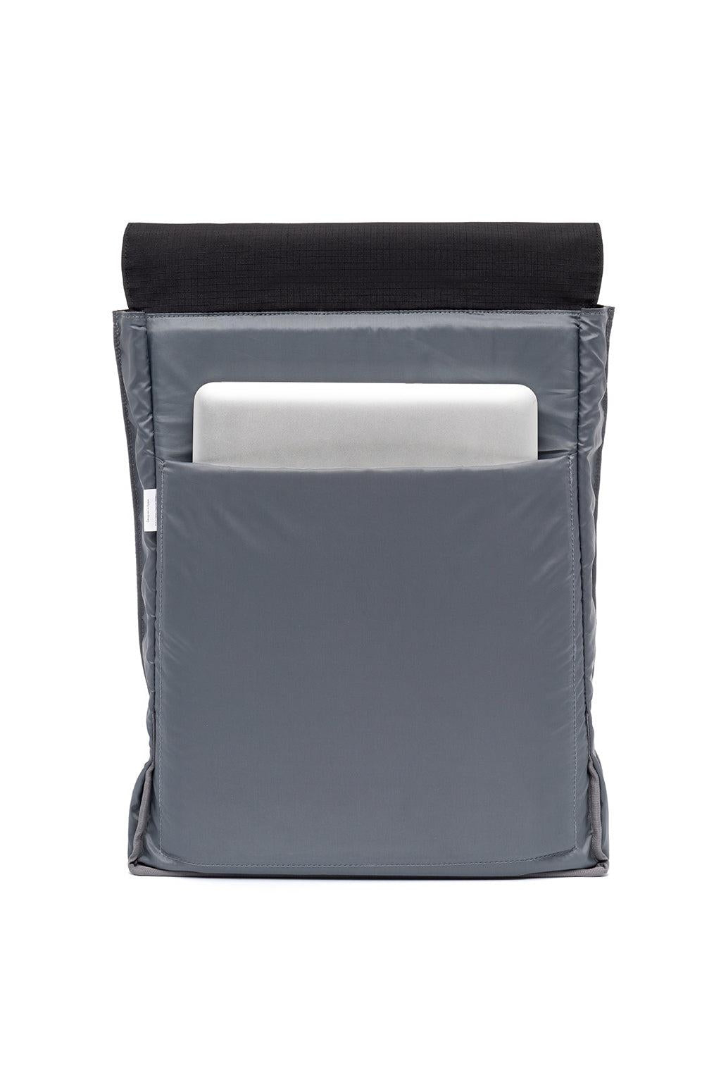 A gray laptop sleeve with a front pocket holding a silver laptop, featuring a black textured fabric panel at the top, shown against a plain white background.