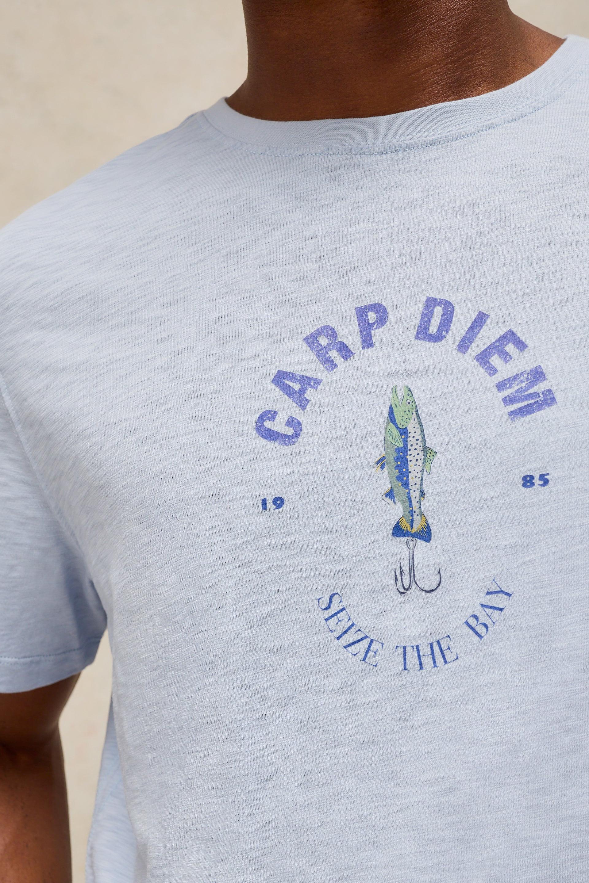 A close-up of a person wearing a light heather gray t-shirt with a blue graphic print featuring a fishing lure and the text 'CARP DIEM' and 'SEIZE THE BAY'.