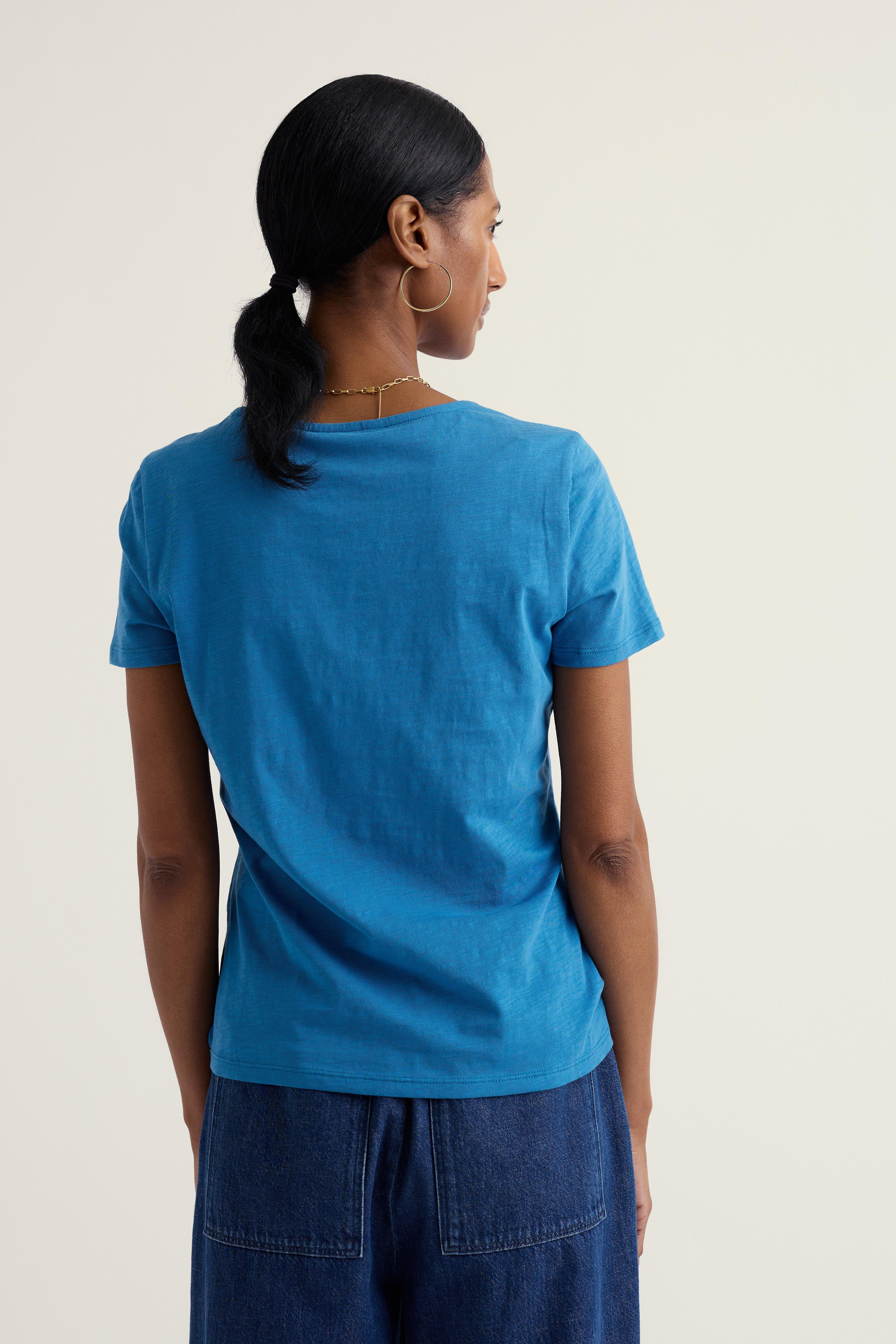 Person wearing a blue organic cotton t-shirt and dark pants on a plain background