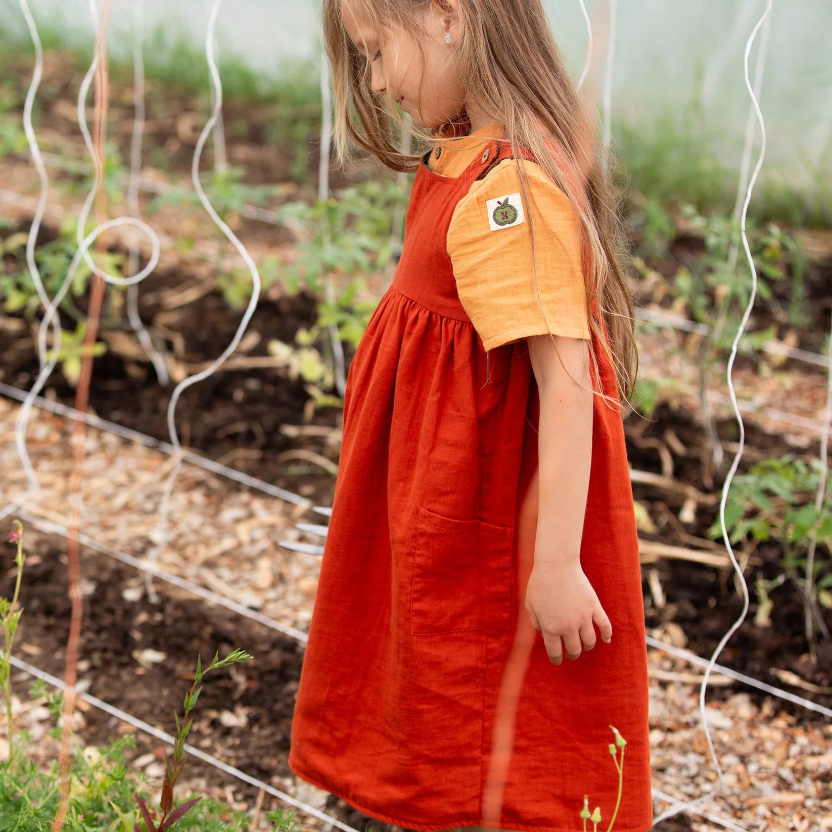 Child in a red dress with an orange shirt standing in a garden