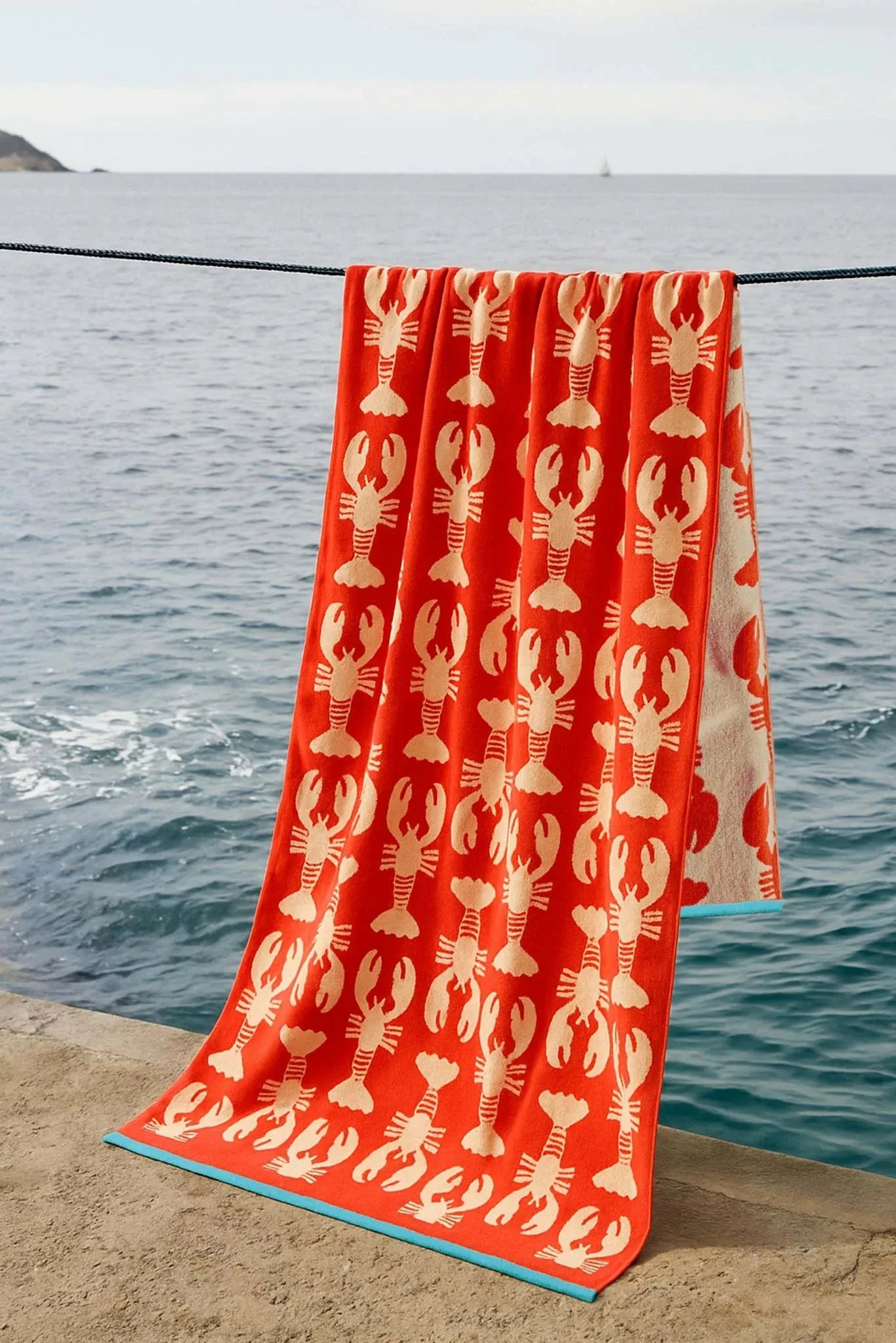 Red towel with lobster pattern on a stone ledge by the water