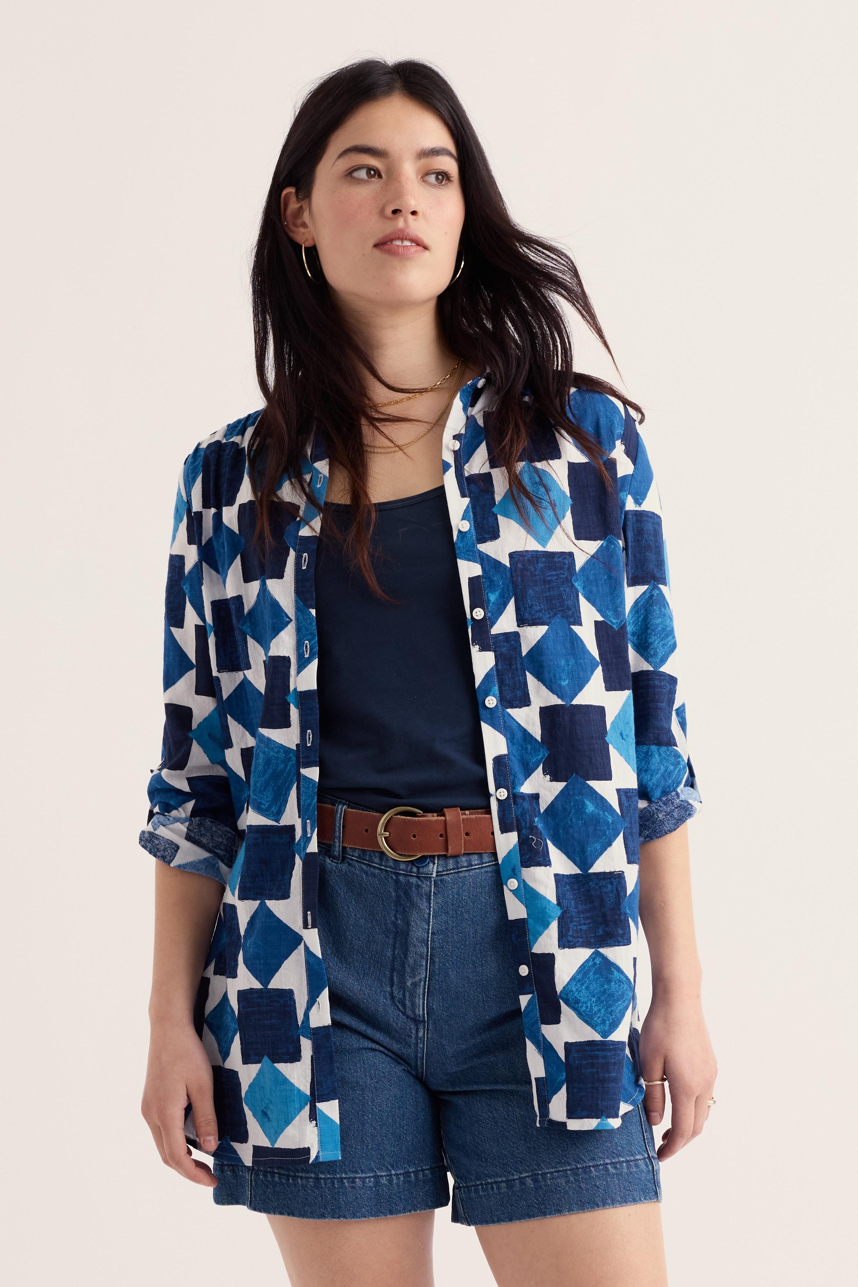 Woman wearing a blue geometric patterned shirt with denim shorts on a beige background