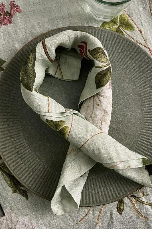 Dining table setting with a green plate, folded napkin, and cutlery on a patterned tablecloth.