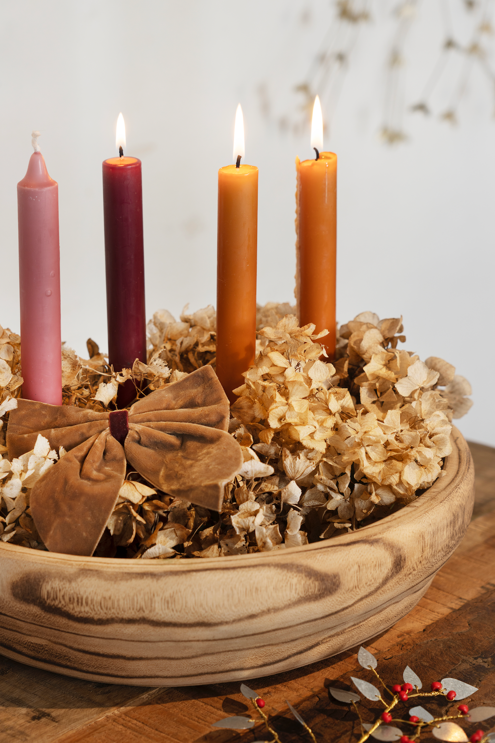 Candle arrangement in a decorative bowl with dried flowers and leaves on a wooden surface.