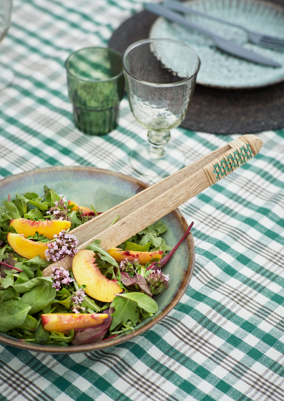 Madam Stoltz bamboo salad tongs resting in a green ceramic bowl filled with fresh peach and arugula salad.