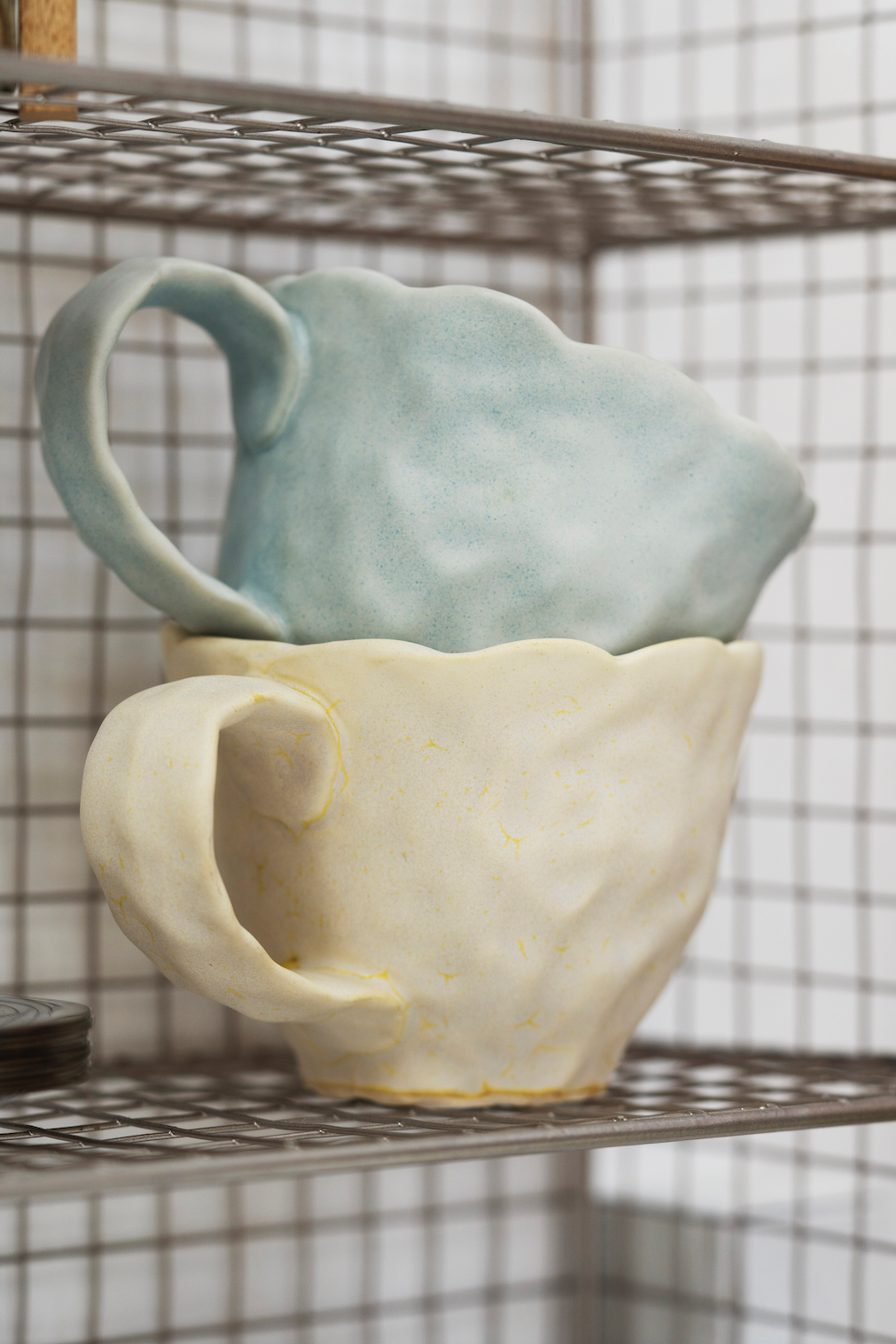 Two ceramic pitchers, one light blue and one white, on a metal shelf.