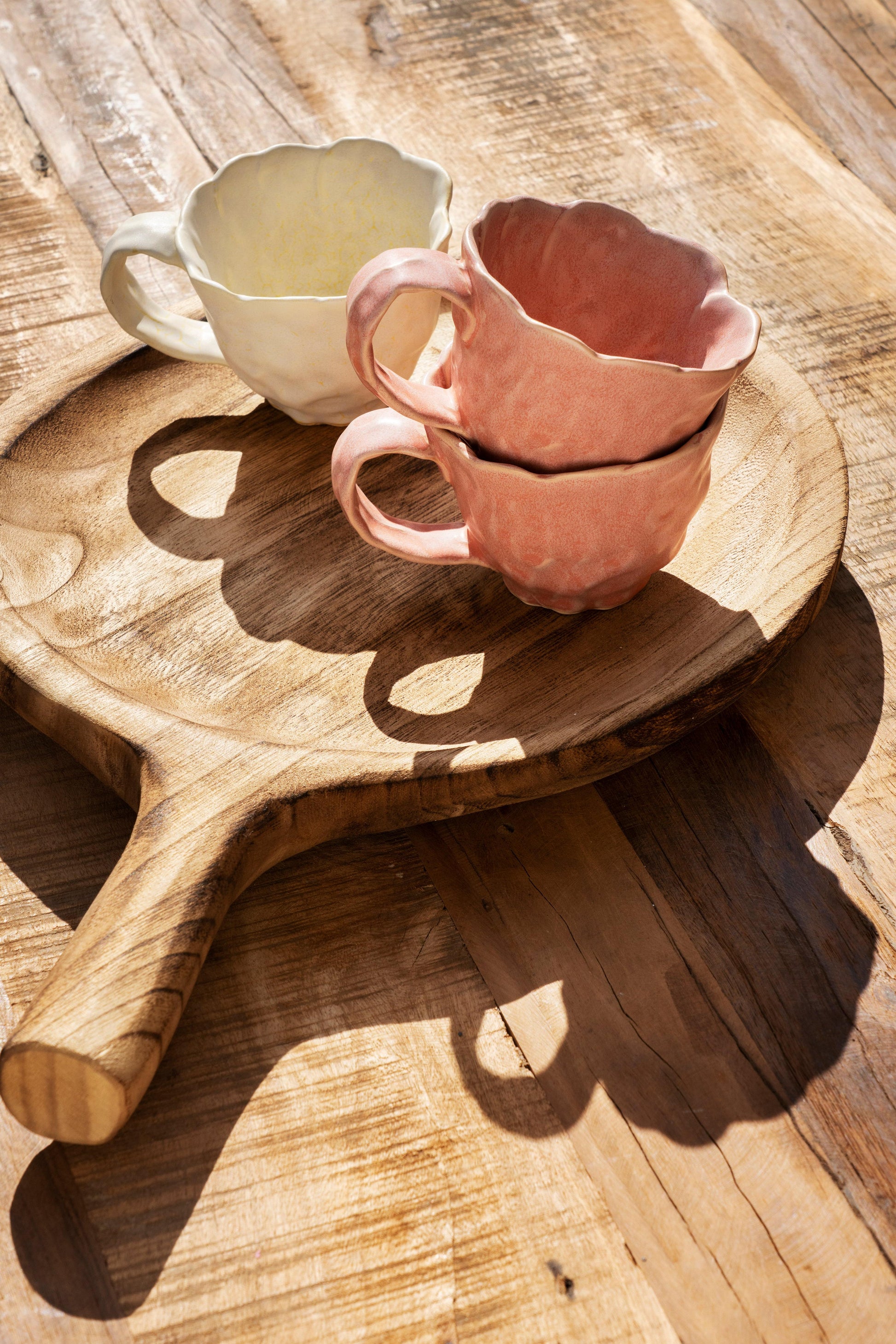 Two ceramic cups on a wooden paddle on a wooden surface