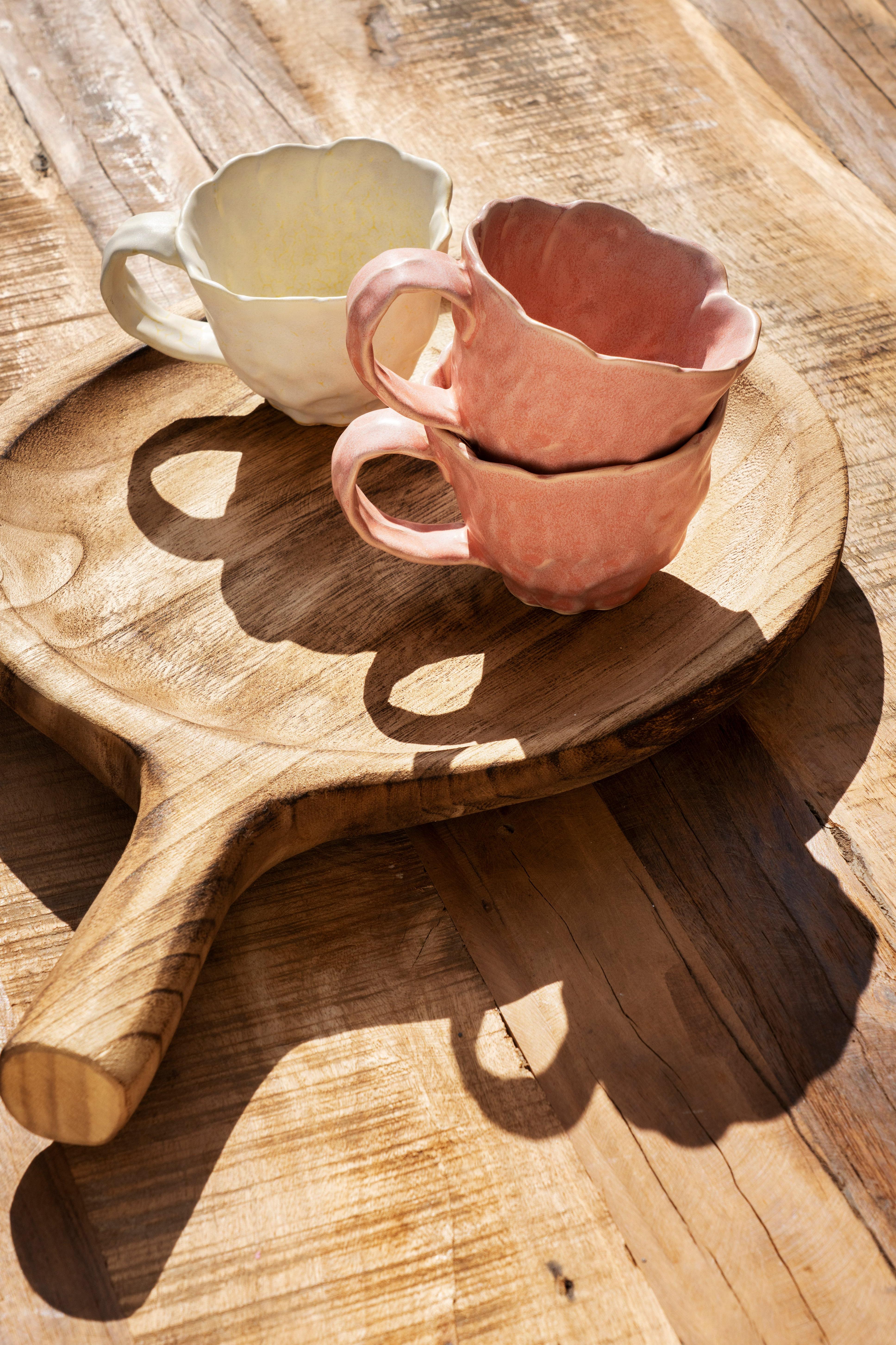 Two ceramic cups on a wooden paddle on a wooden surface