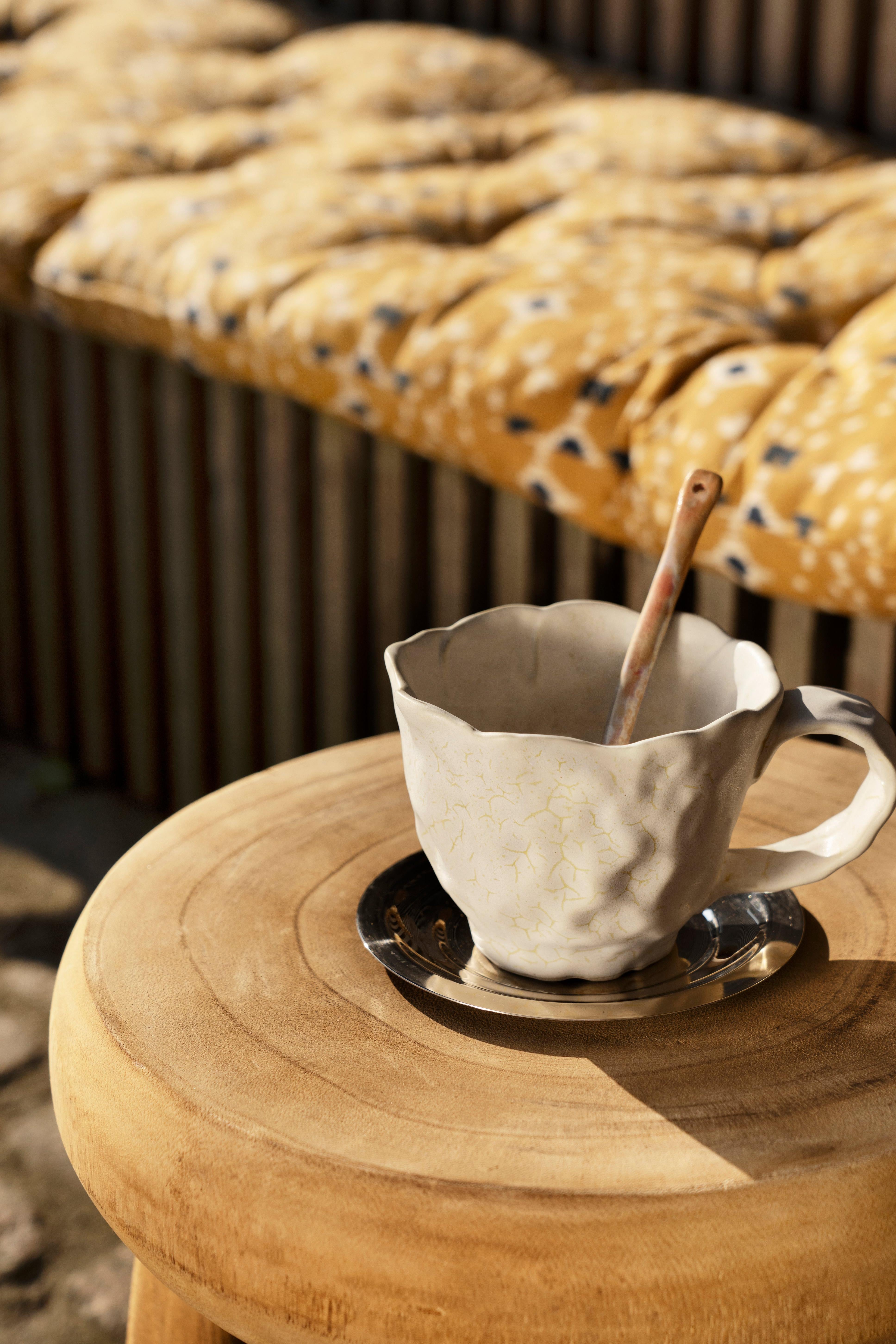 White ceramic cup with a wooden spoon on a wooden stool with a cushioned bench in the background