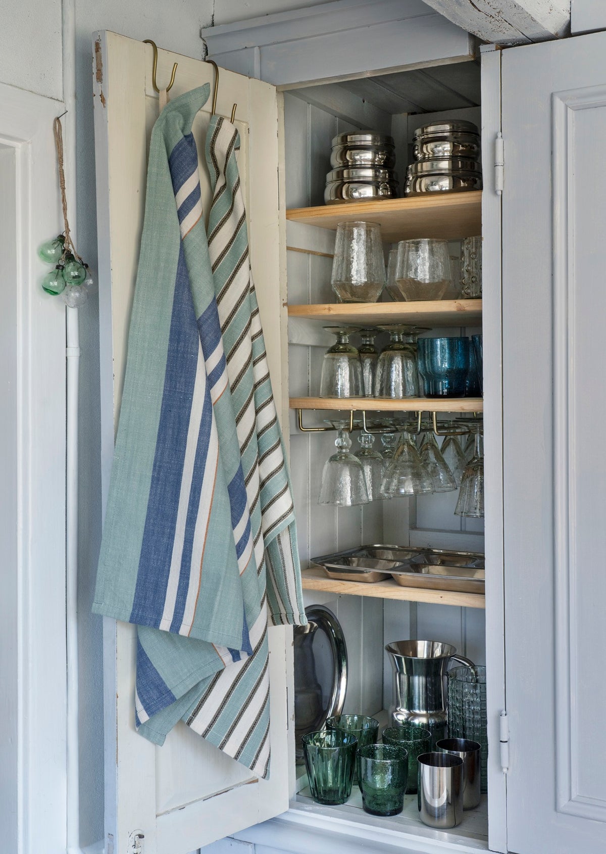 Striped cotton kitchen towel by Madam Stoltz hanging on the door of a kitchen cupboard filled with glassware.