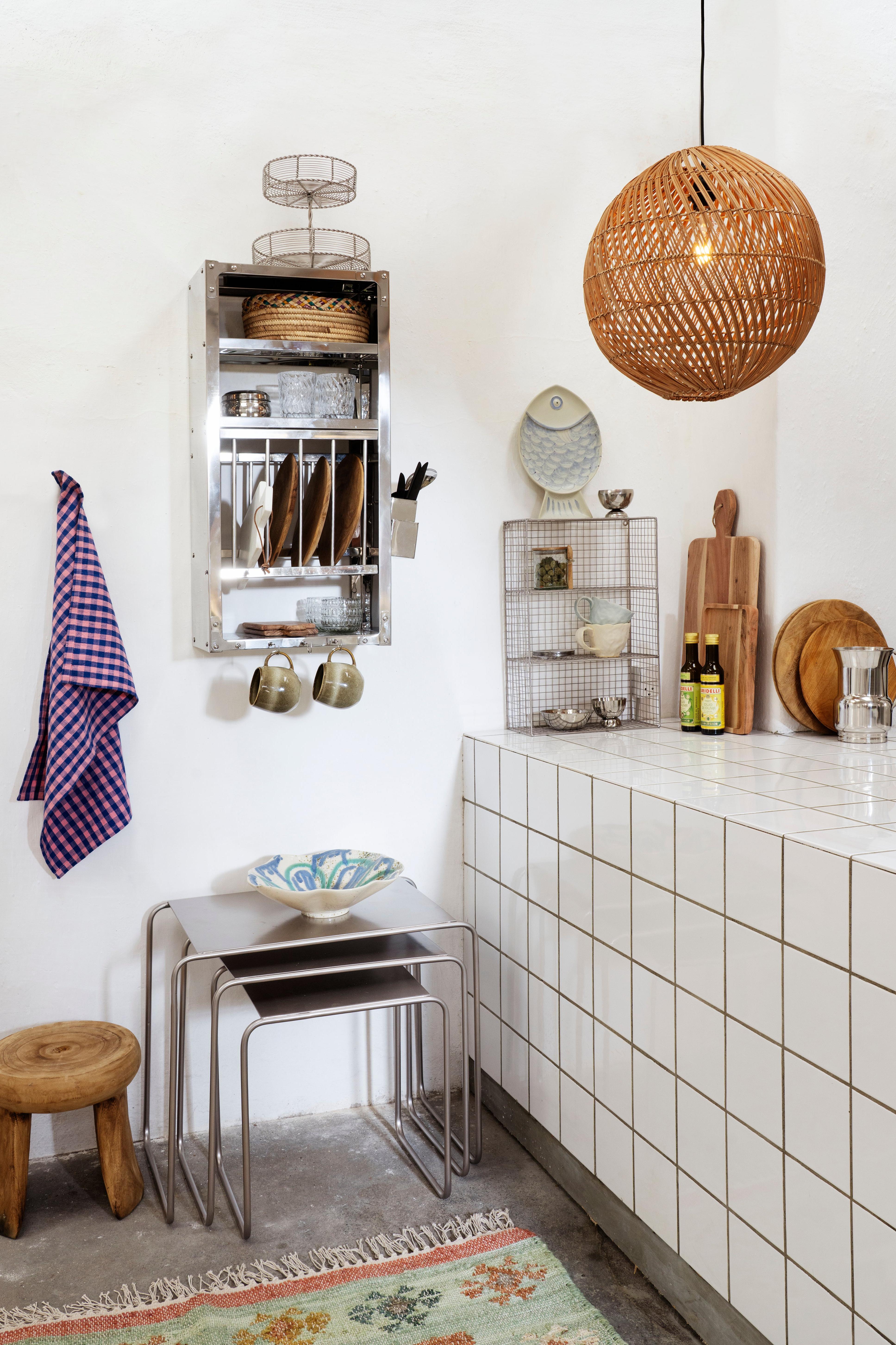 Modern kitchen with white tiled wall, wooden stool, and hanging wicker lamp.