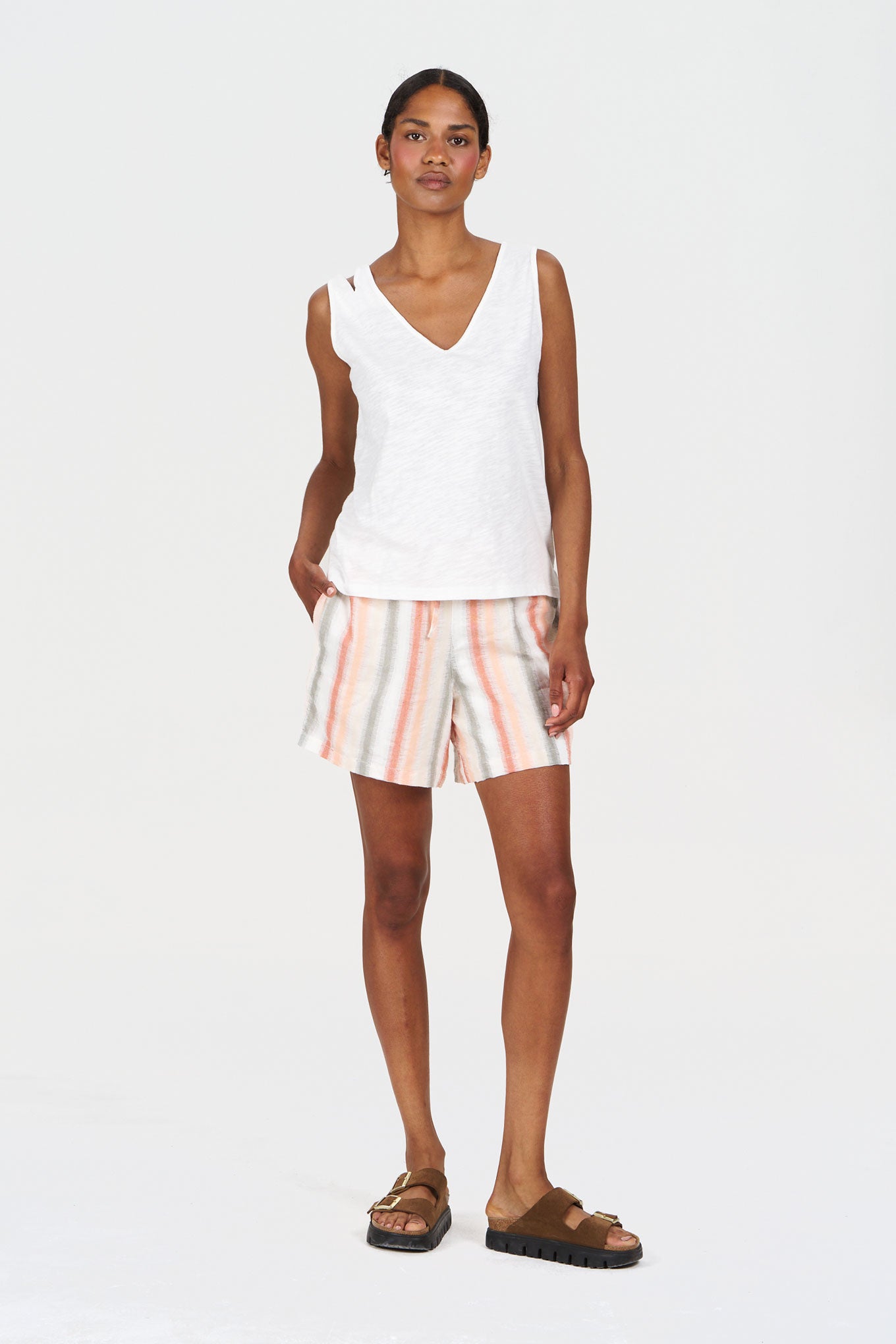 Woman wearing a white sleeveless top and striped shorts on a white background