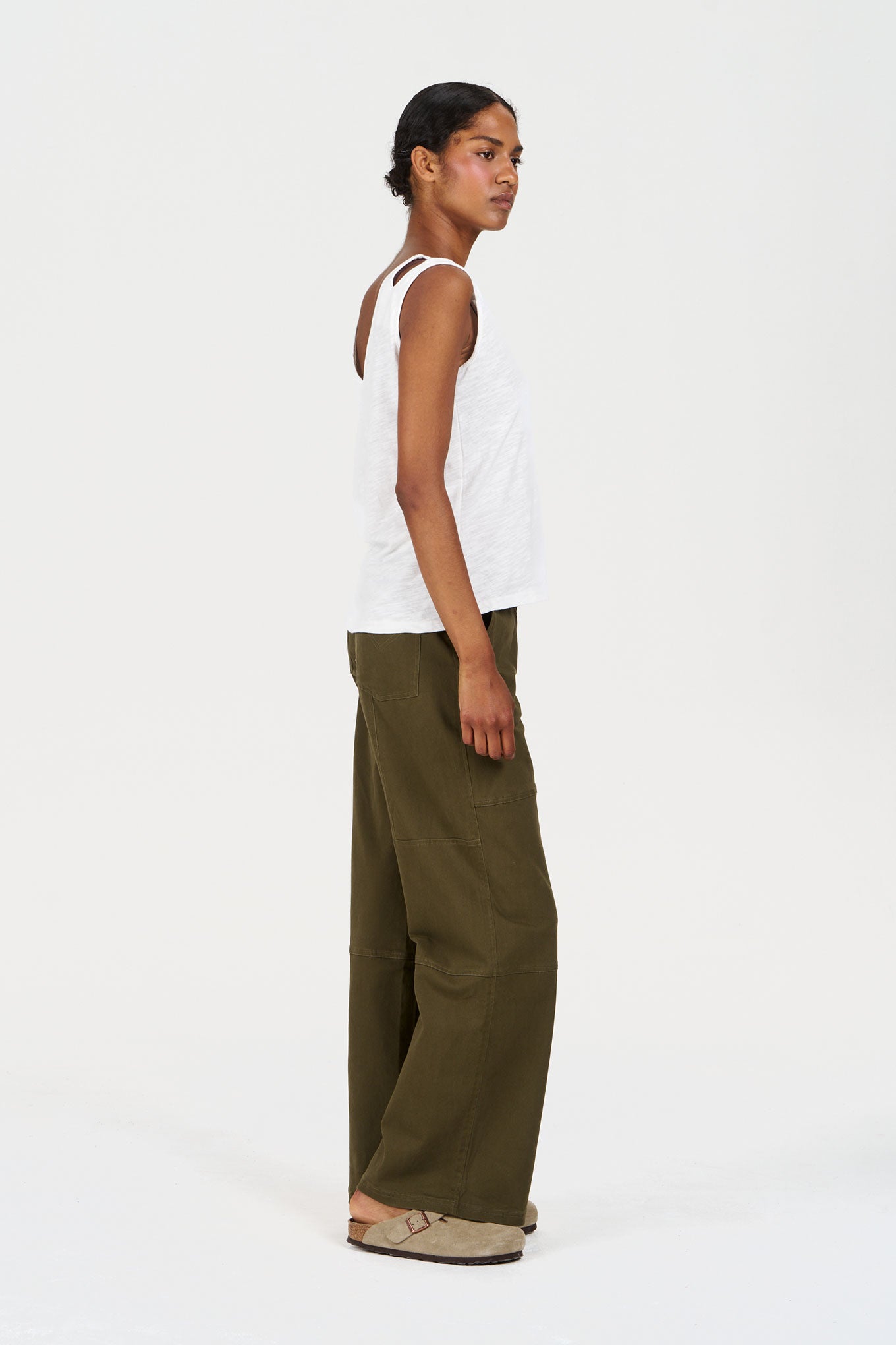 Person wearing a white sleeveless top and olive green pants on a white background