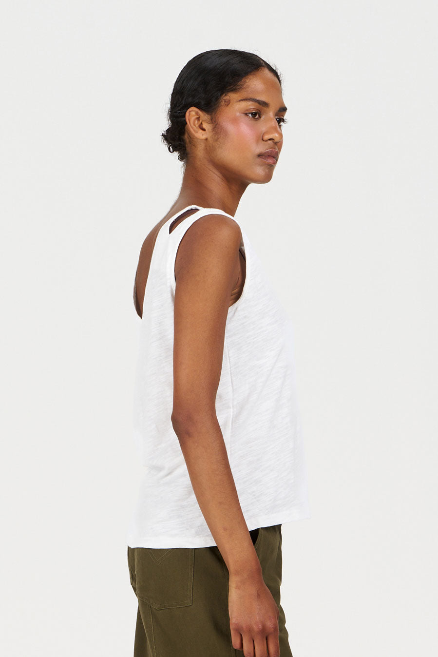 Woman wearing a white tank top and green pants on a white background