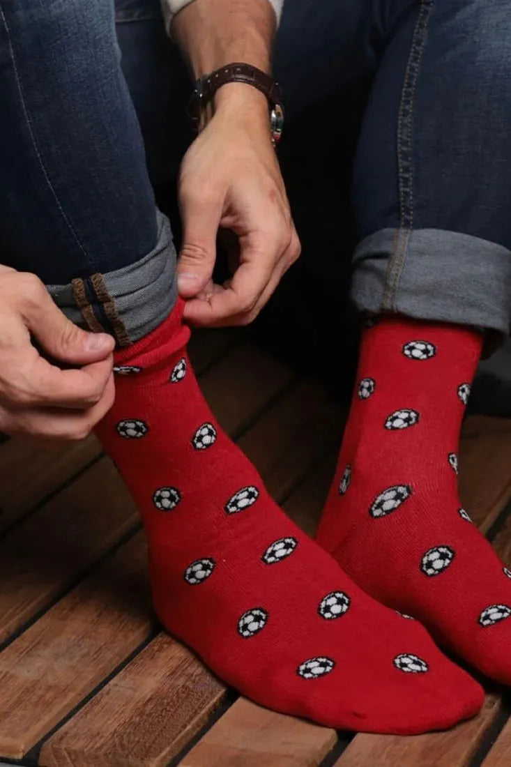 A man wearing blue cuffed jeans adjusting bright red socks with soccer ball patterns.