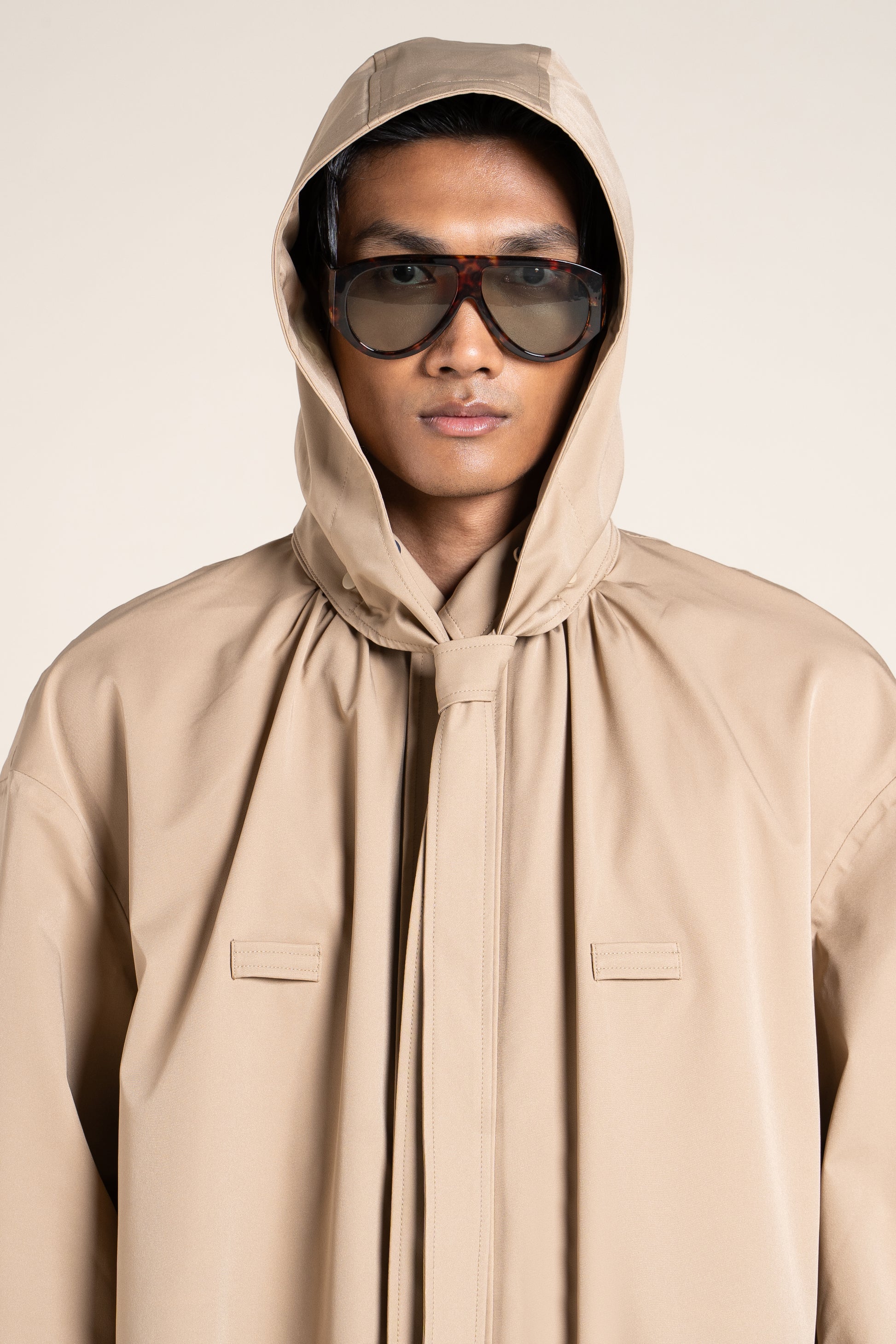 A man wearing a stylish beige Flotte waterproof coat with a hood and tortoiseshell sunglasses.