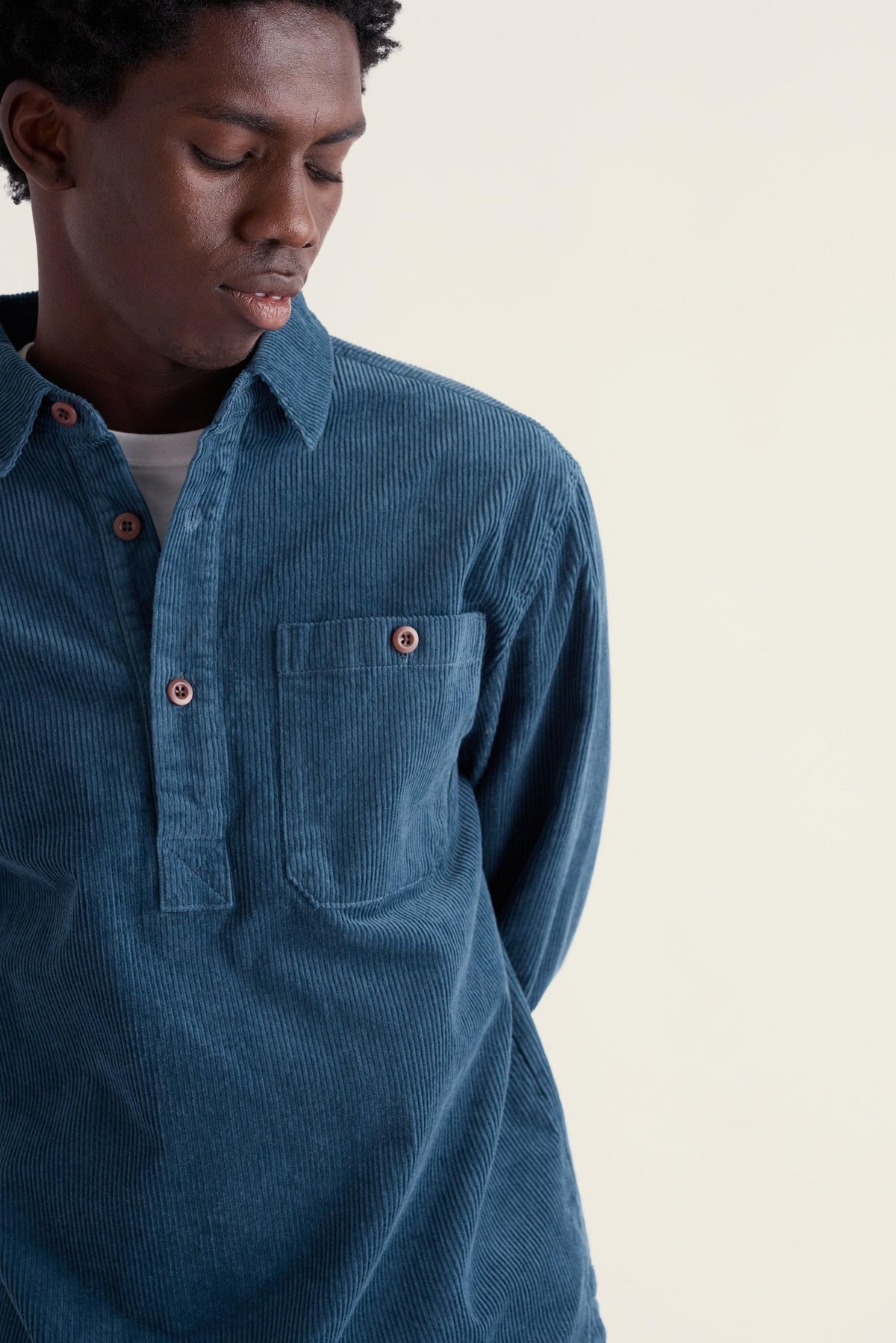 A man wearing a blue corduroy pullover casual shirt against a light background.