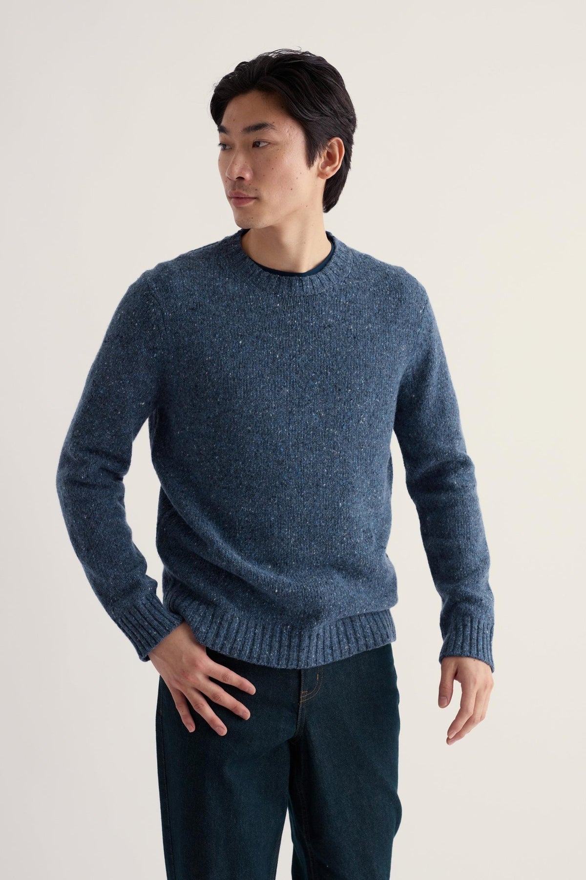 A man wearing a blue merino wool knitwear sweater, posing against a neutral studio background.