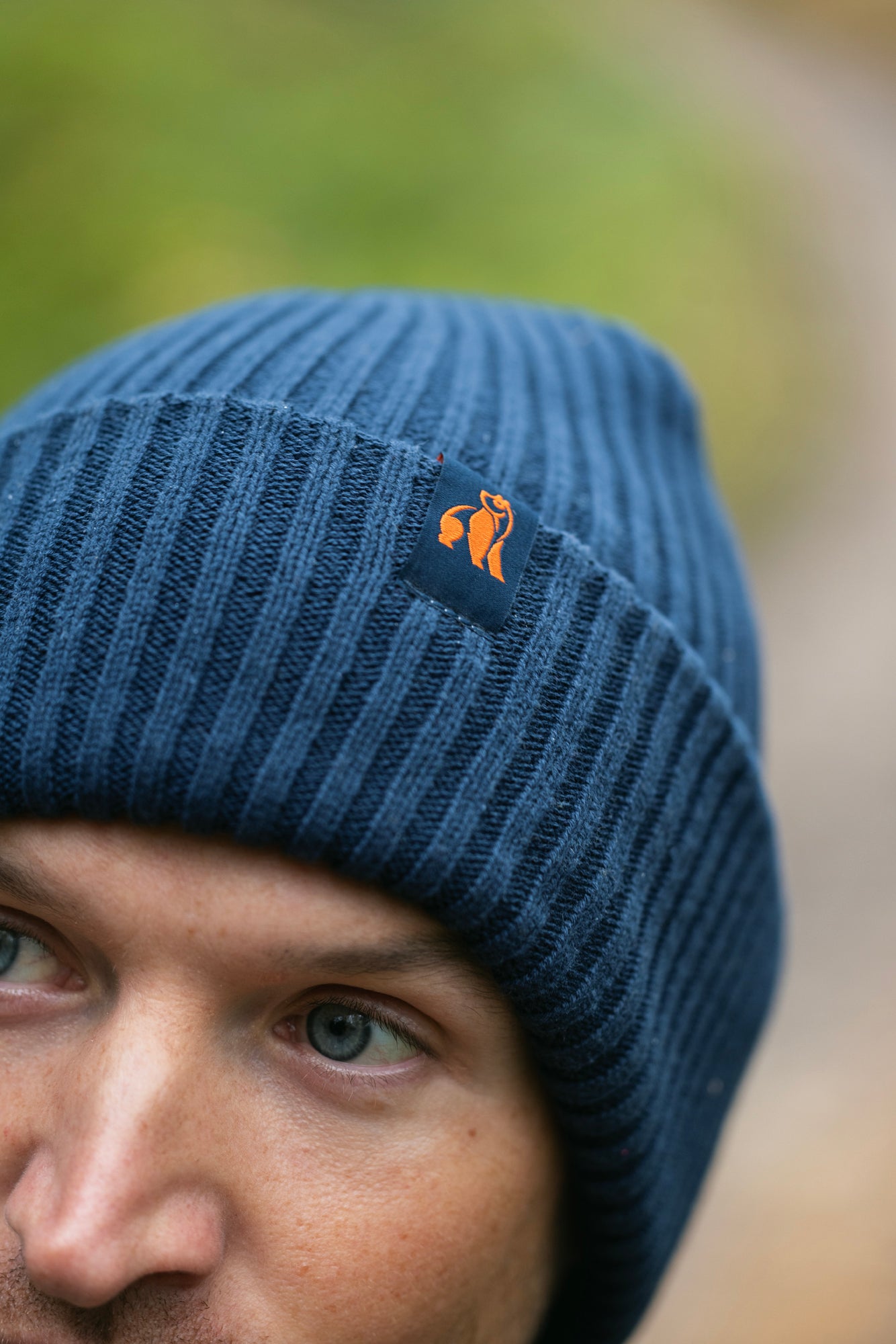Close up of a man wearing a blue organic cotton beanie with a Swole Panda logo tag.