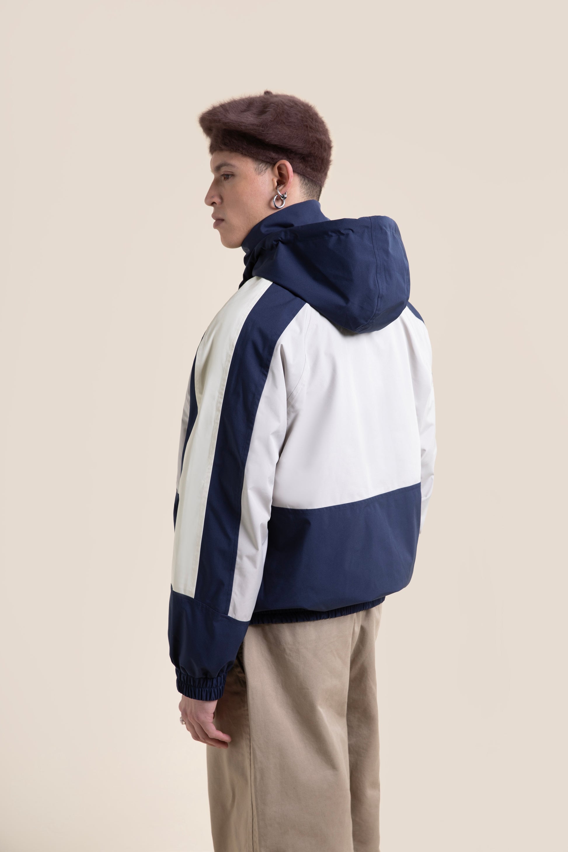 A man wearing a blue and white waterproof jacket against a light beige background.