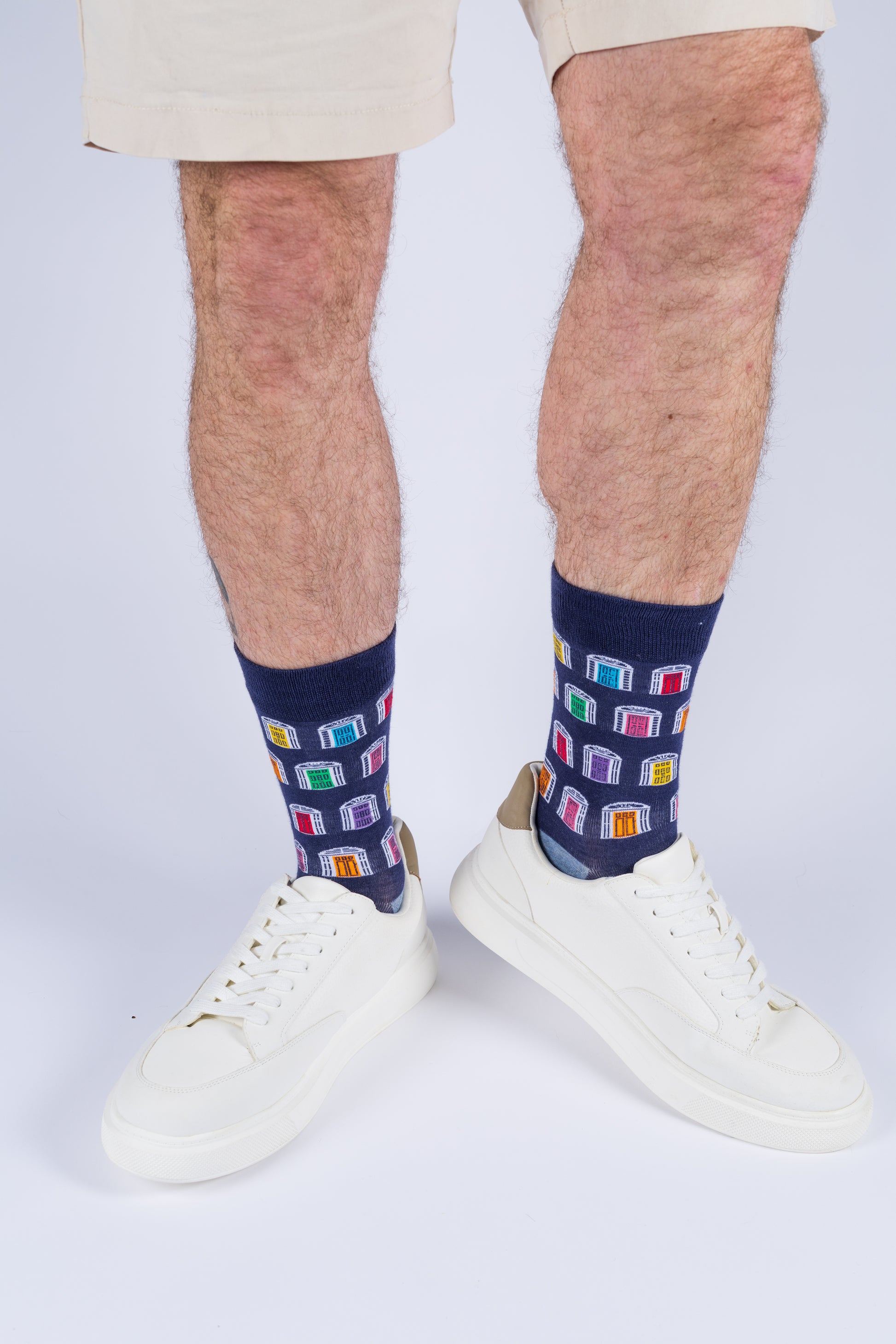A man wearing navy blue socks with a colorful door pattern and white sneakers against a white background