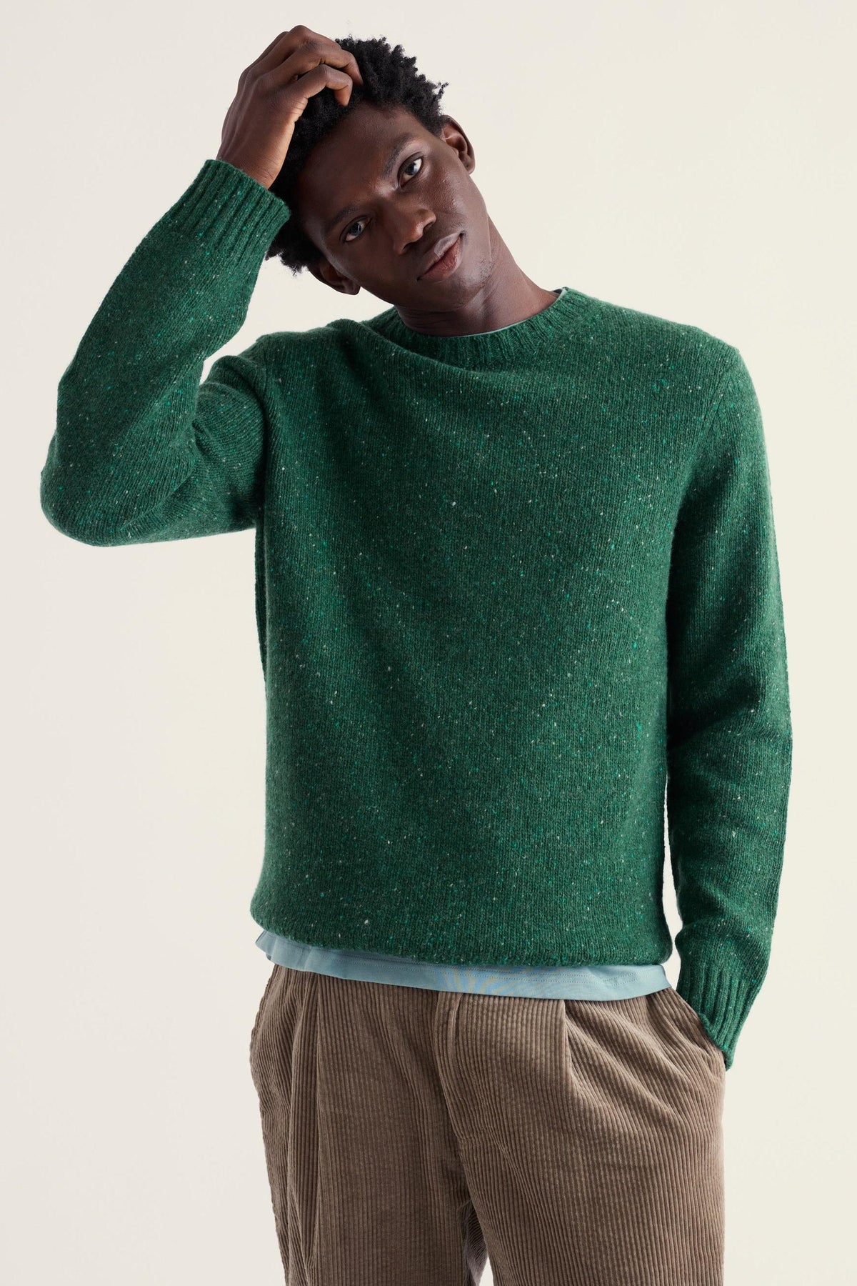 A man wearing a green merino wool sweater posing with his hand on his head against a light background.