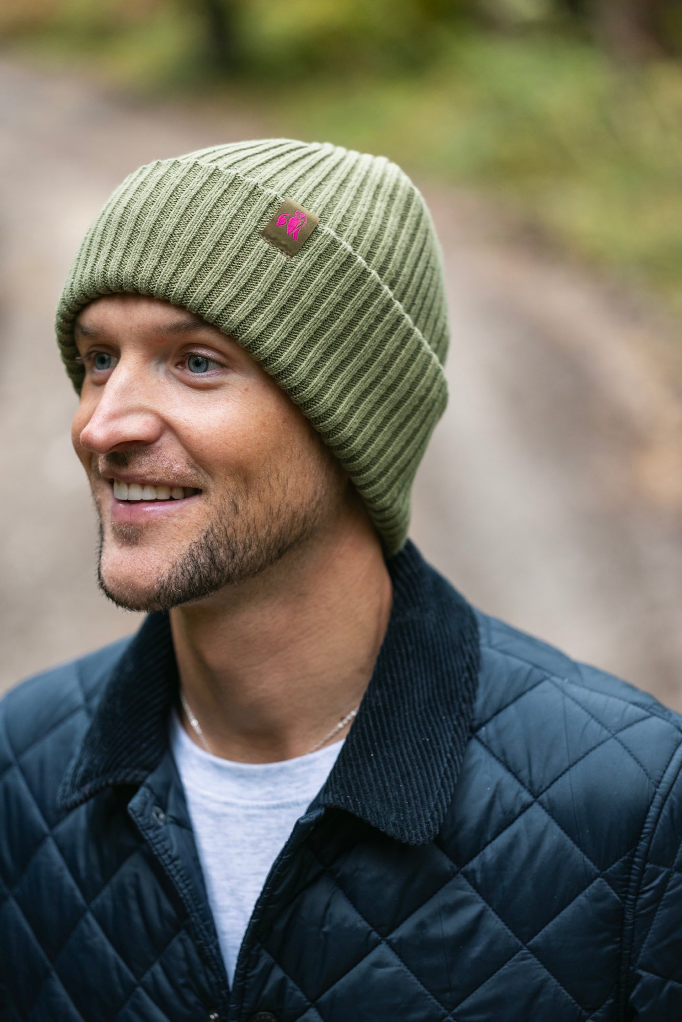 Man wearing a green knit beanie with a pink logo outdoors