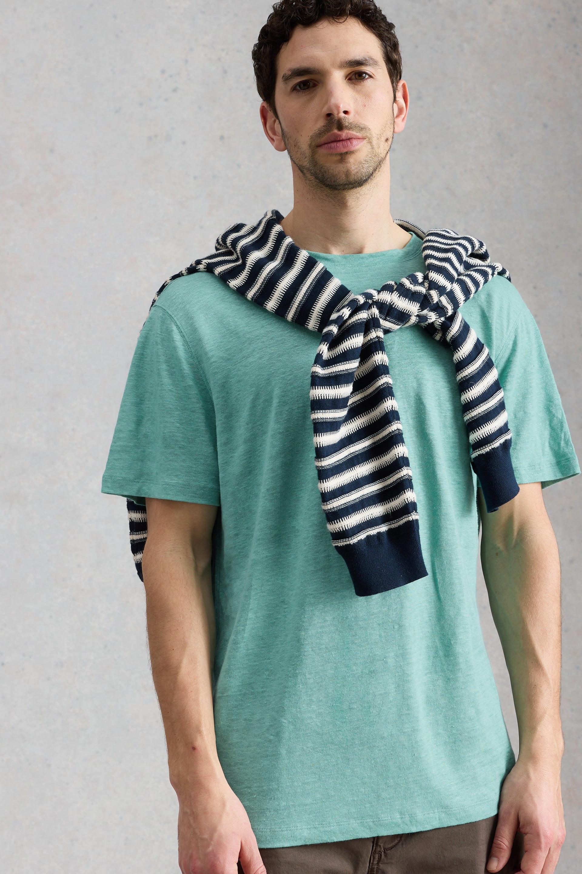 Man wearing a green linen t-shirt with a striped jumper draped over his shoulders