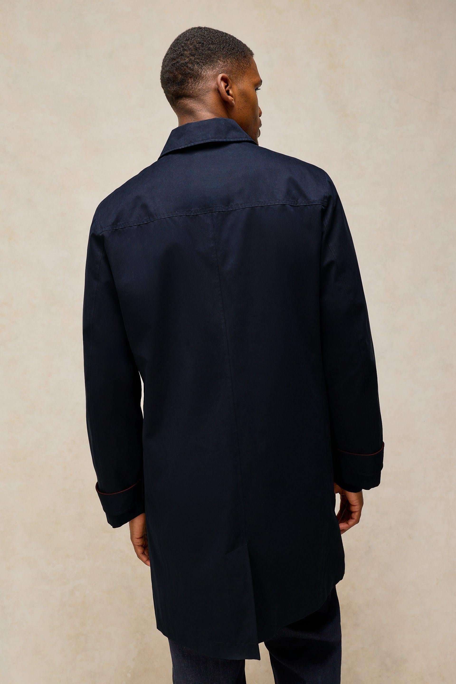 A man viewed from the back wearing a dark navy blue longline shirt jacket or coat, set against a textured beige studio background.